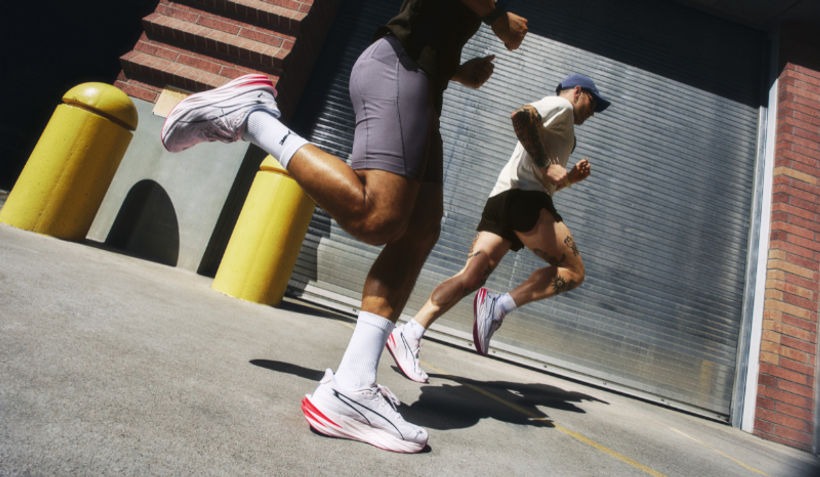 Two runners in white sneakers with red accents ascend an urban incline.