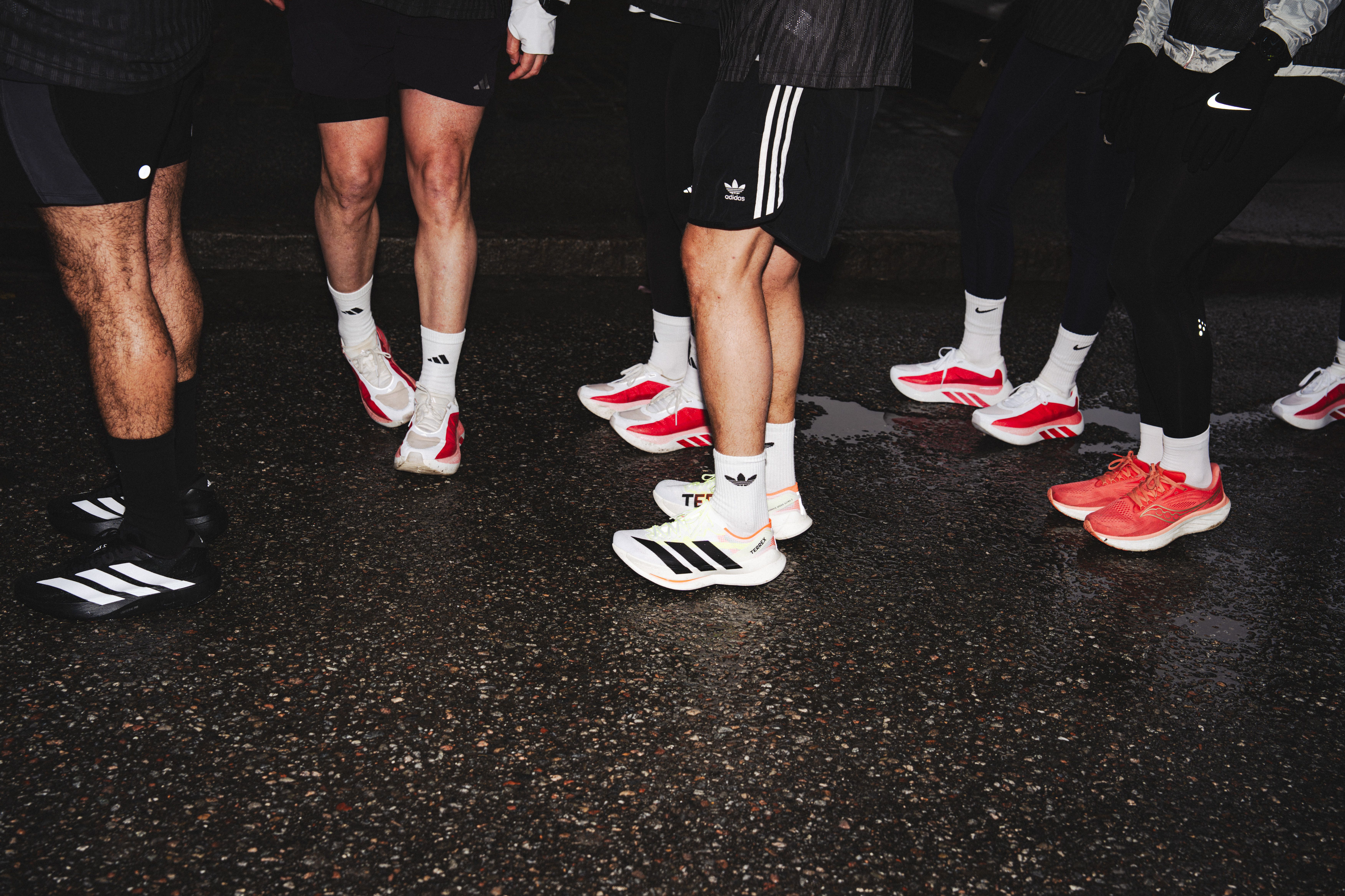 Multiple people wearing various Adidas running shoes on a wet street.