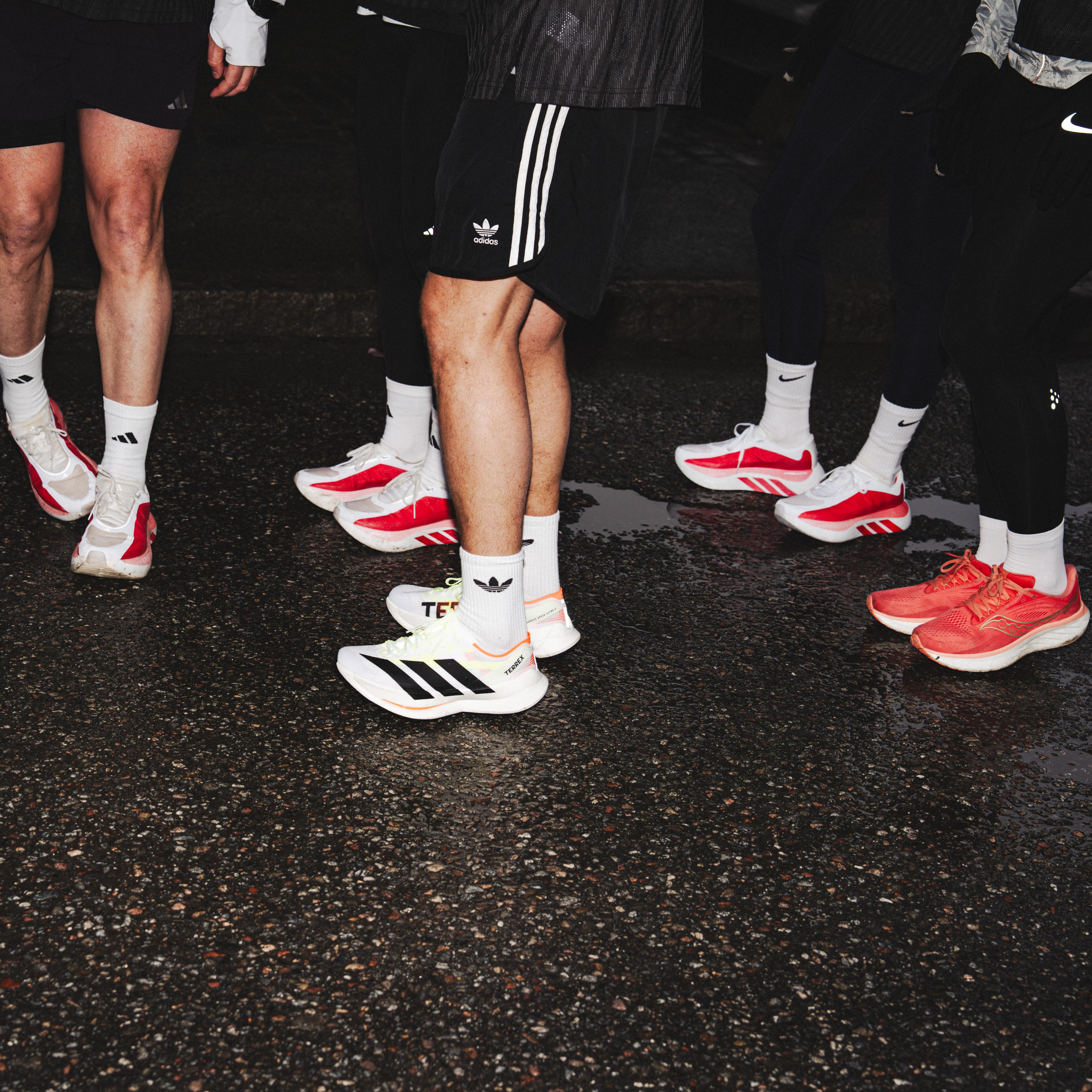 Multiple people wearing various Adidas running shoes on a wet street.
