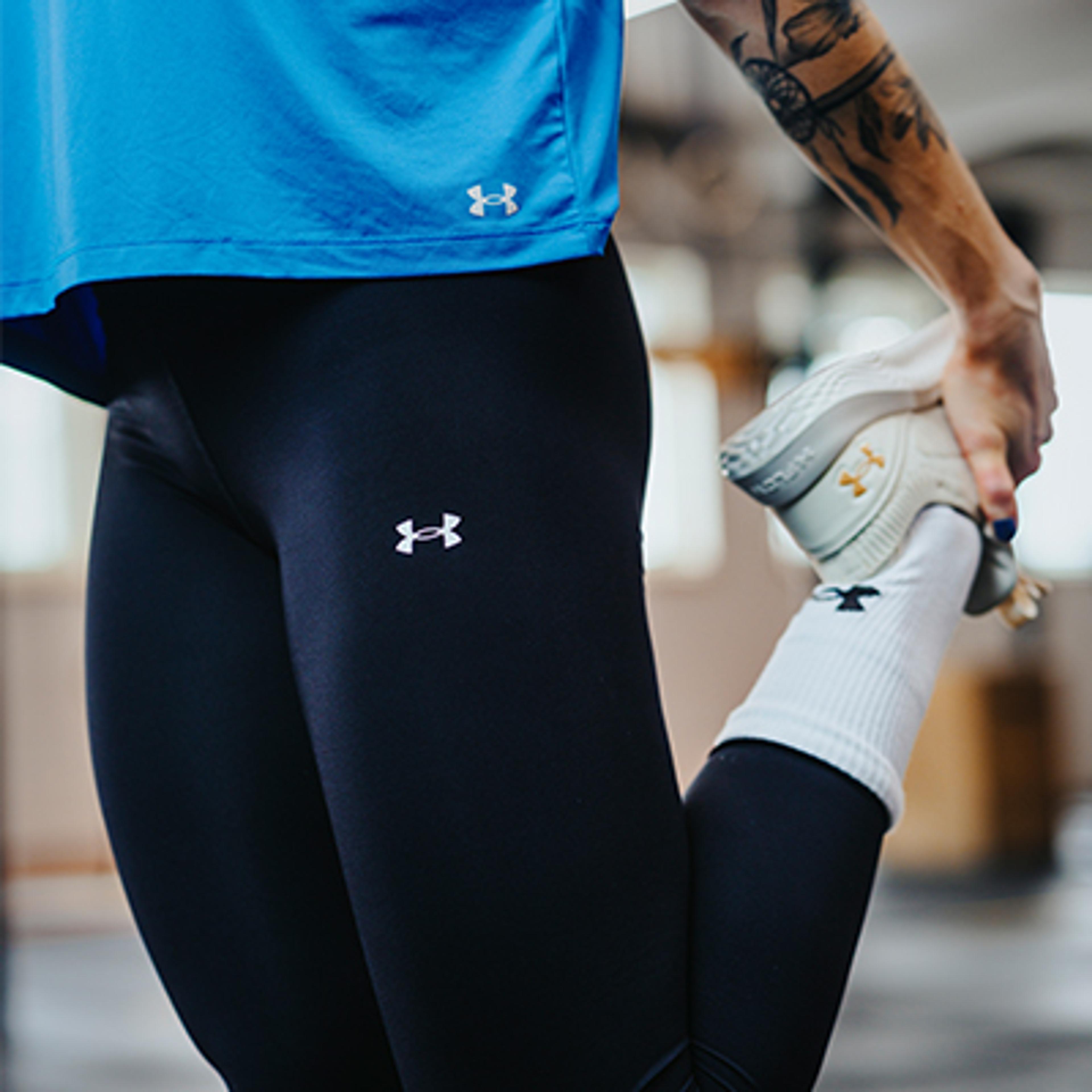 a person wearing under armour leggings and a blue shirt is stretching their leg .