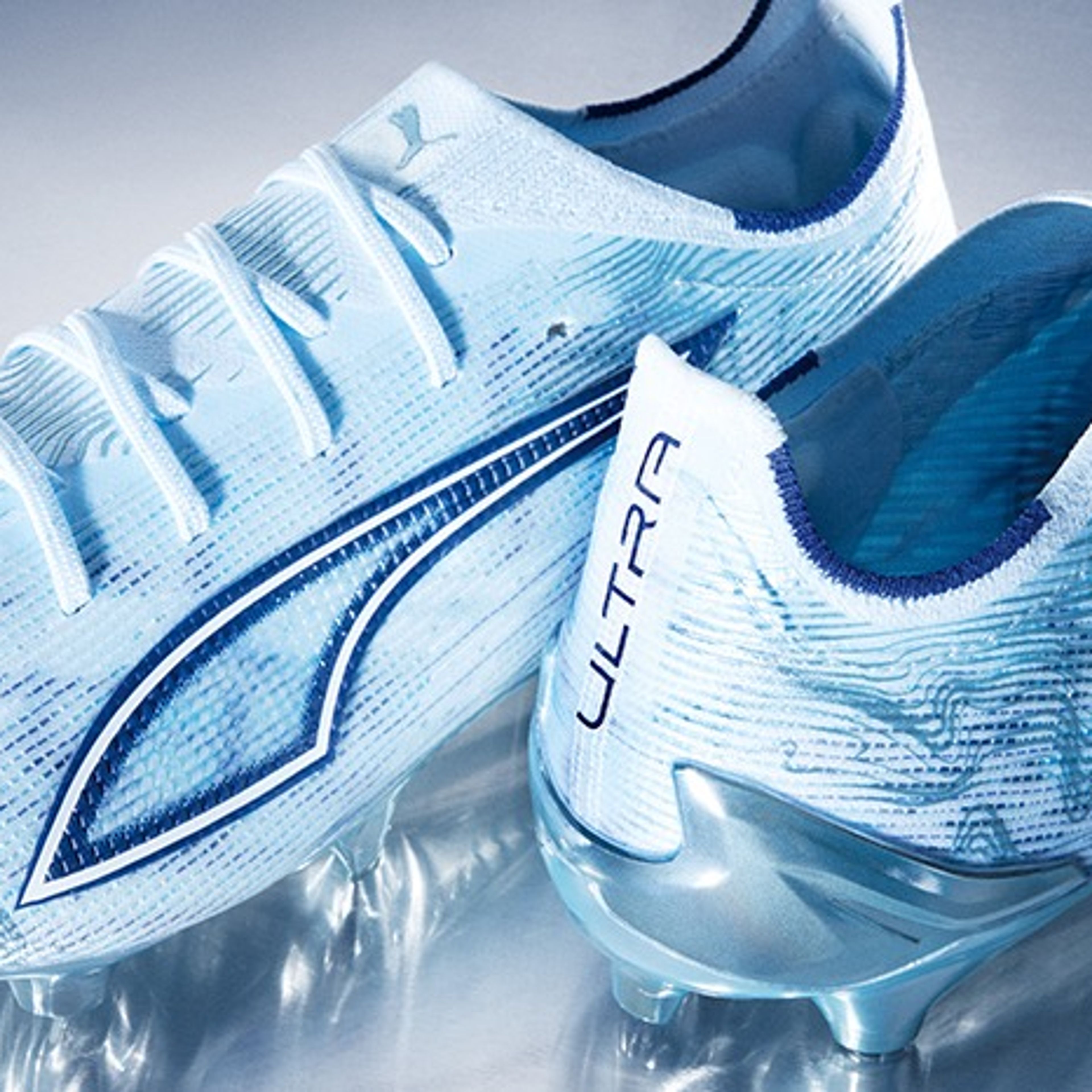 Two light blue Puma Ultra football boots with a wavy pattern on a reflective surface.