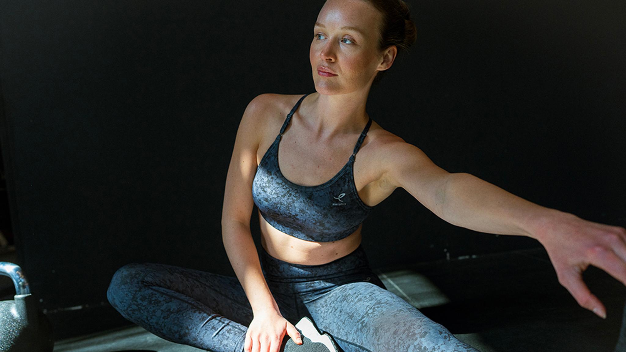 a woman in a sports bra and leggings is sitting on the floor with her arms outstretched .