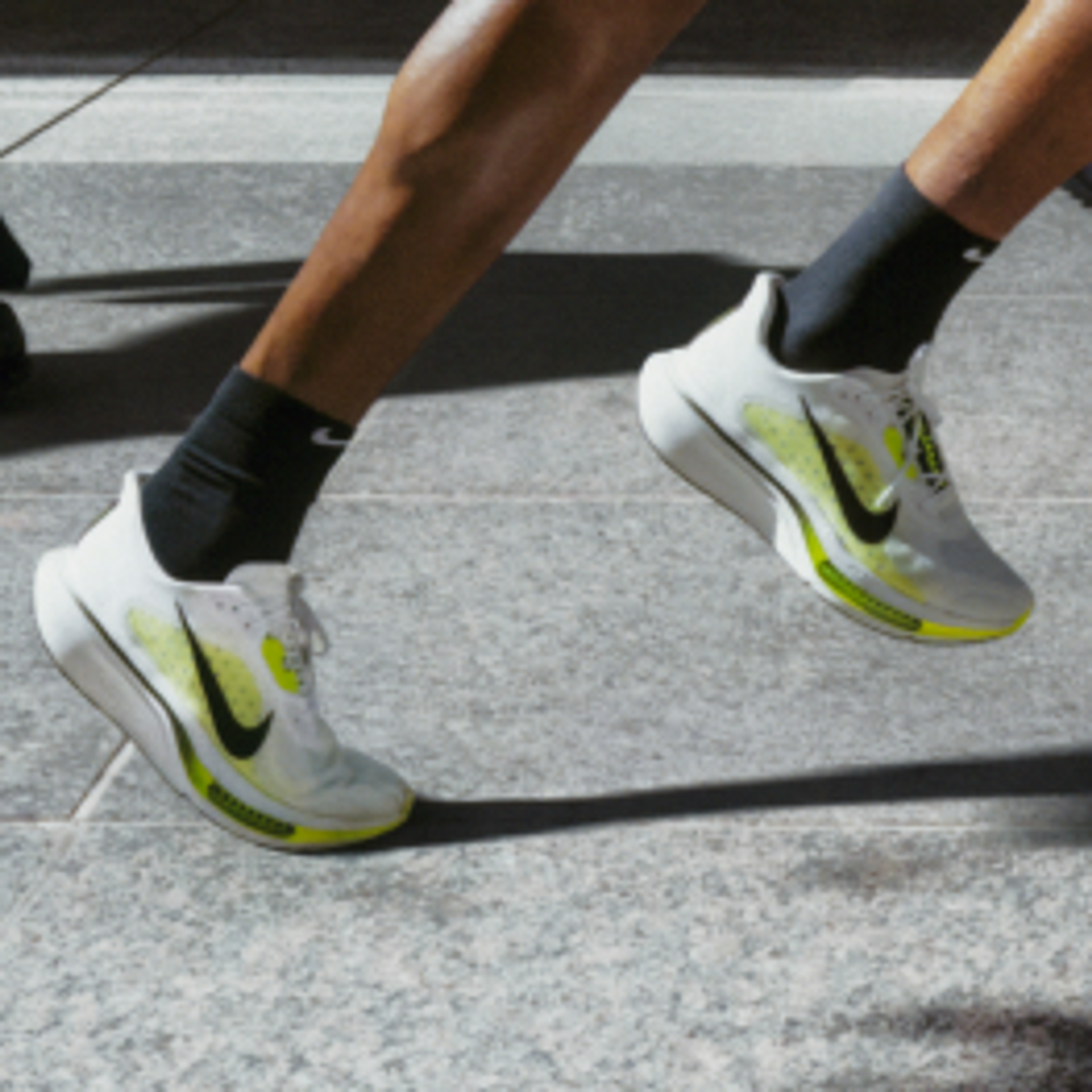 Runner in bright athletic shoes strides past pedestrians on a city sidewalk.