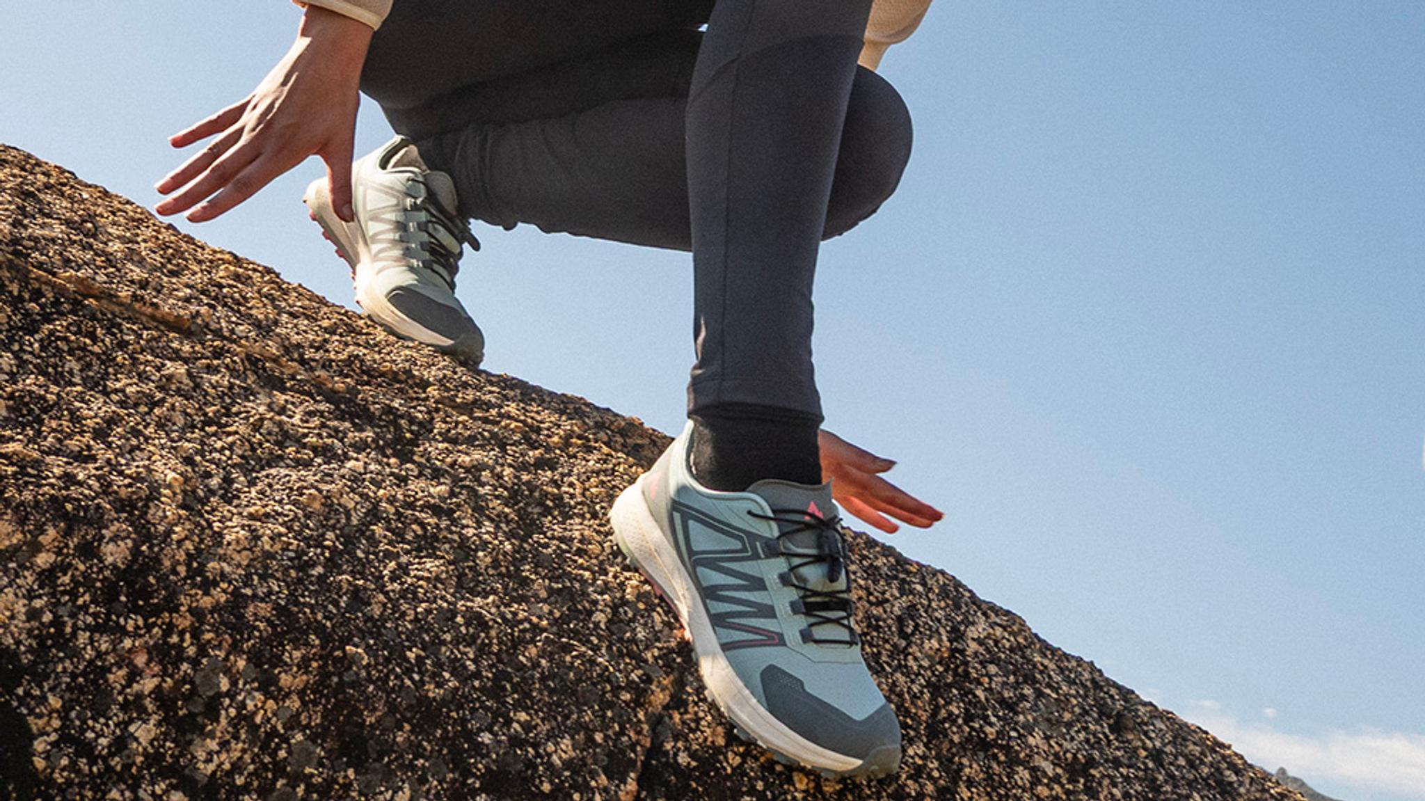 Person wearing light blue trail running shoes climbing a rock.