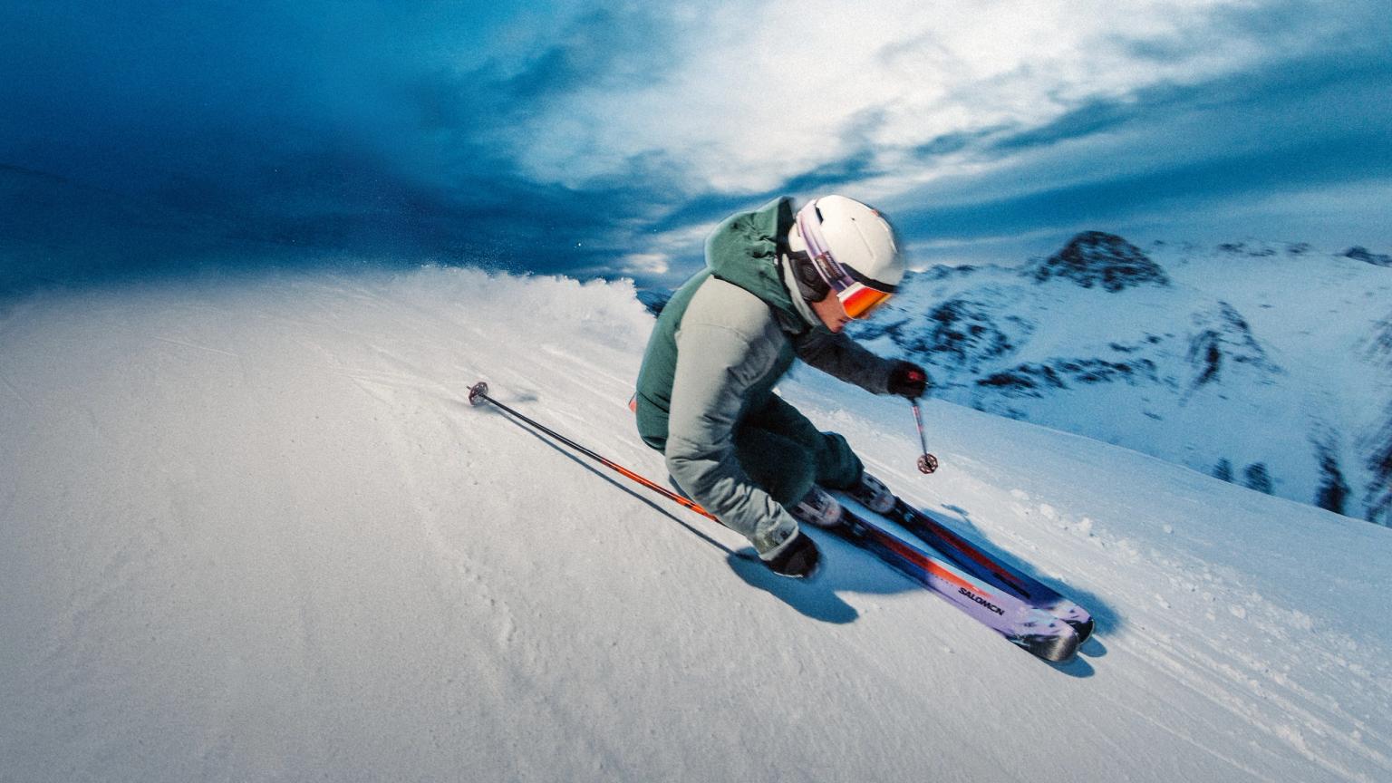 Skier carving a turn on a snowy mountain slope under a dramatic blue sky.