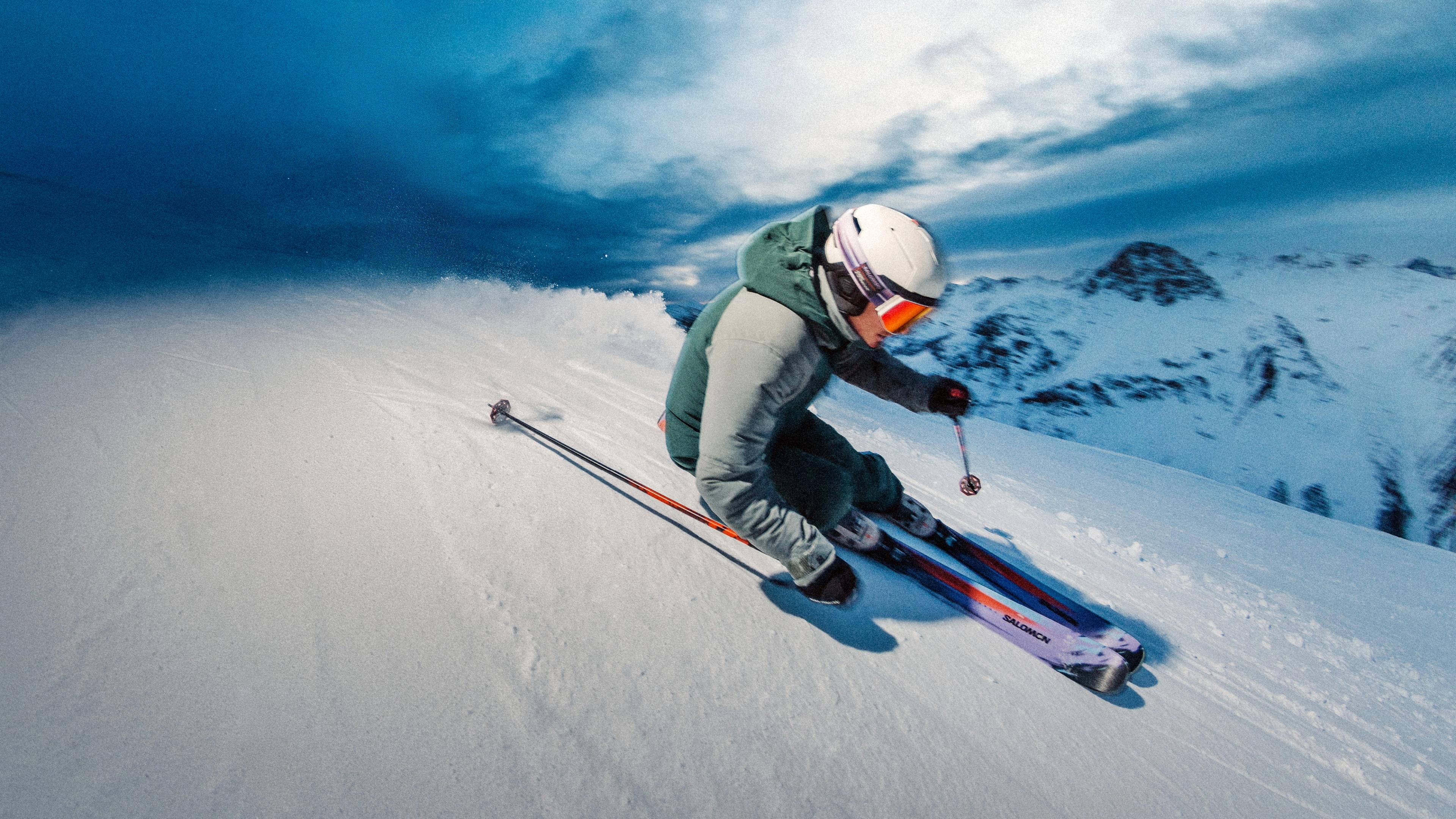 Skier carving a turn on a snowy mountain slope under a dramatic blue sky.