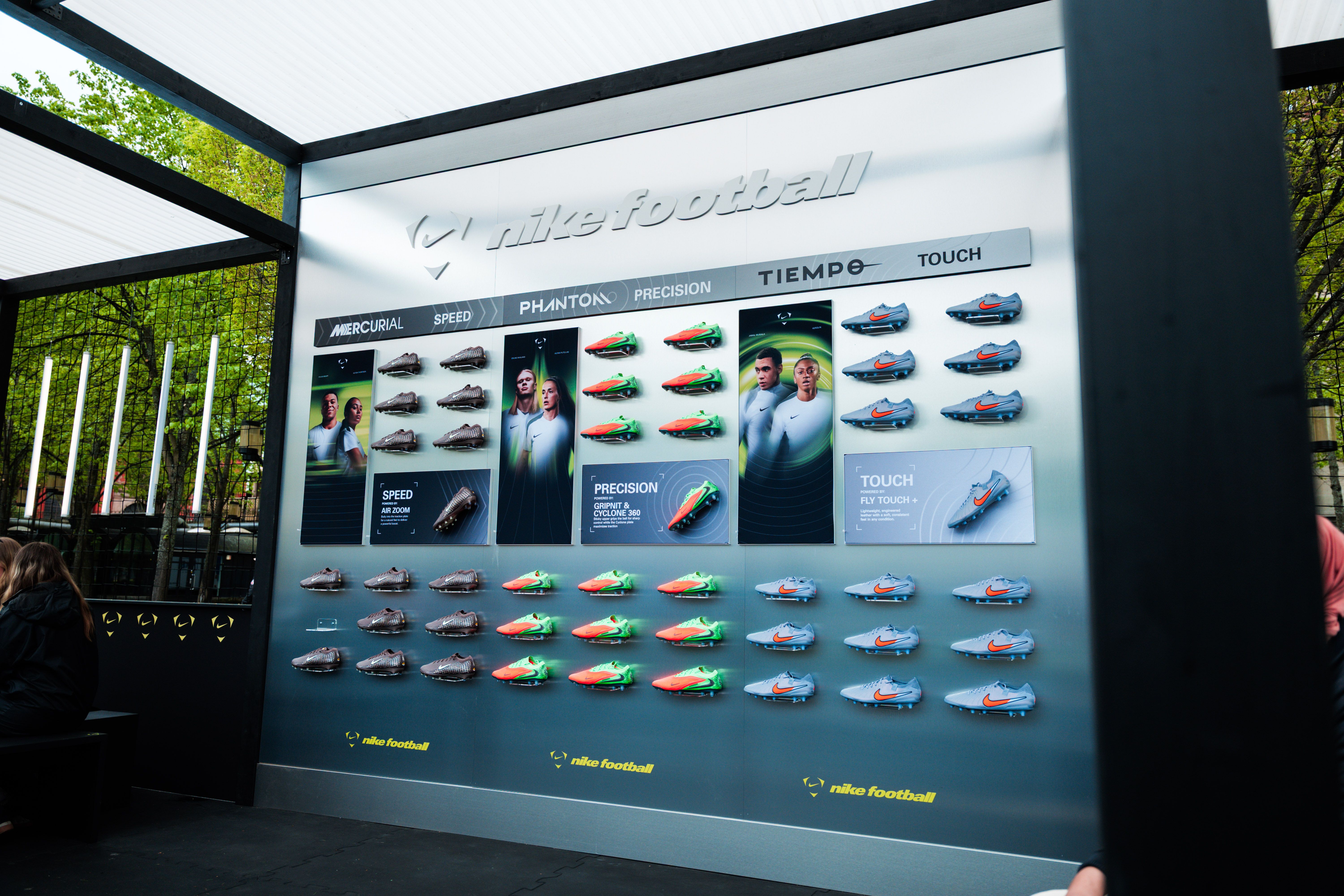 An outdoor Nike Football display wall showcasing rows of different football boot models, product categories, and athlete images.