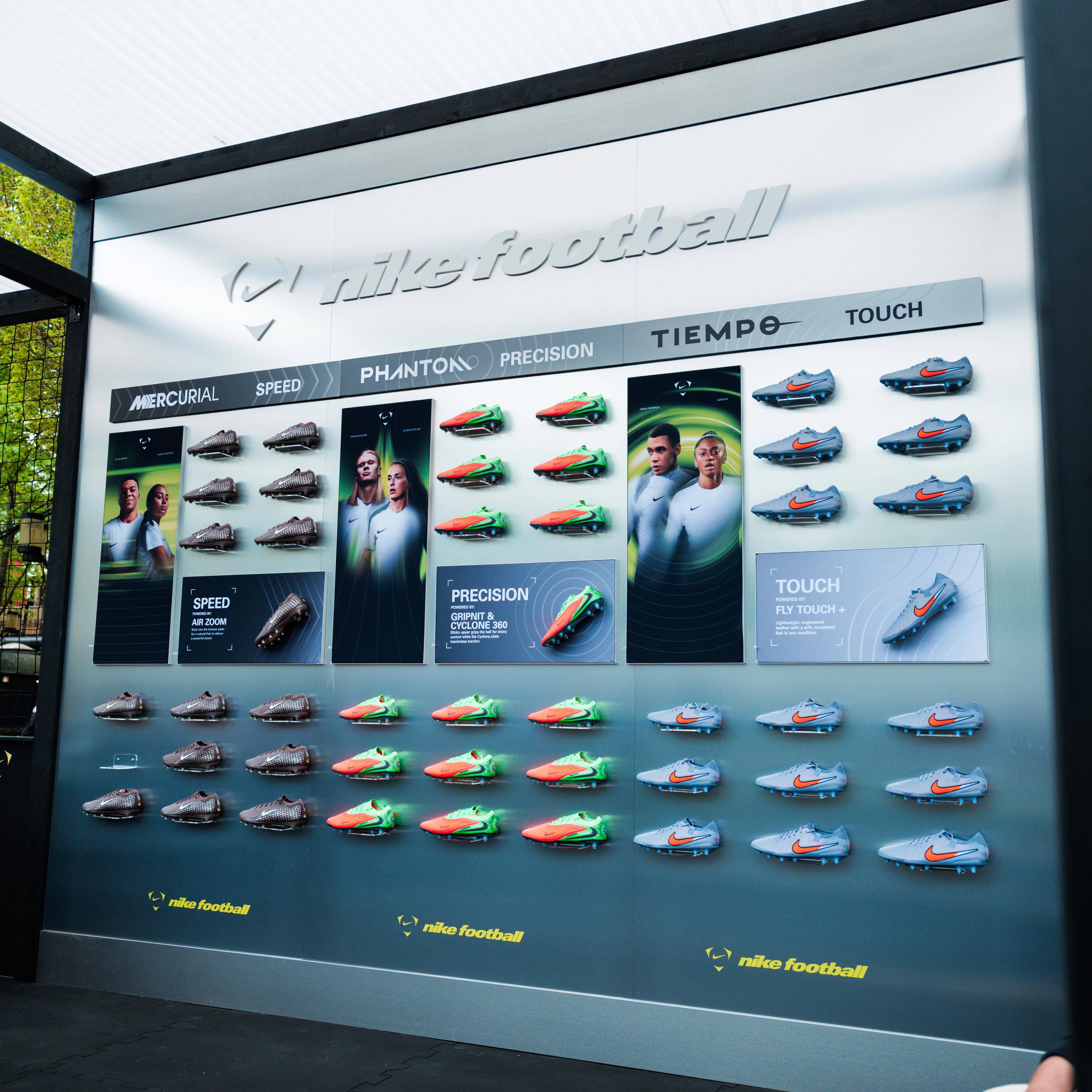 An outdoor Nike Football display wall showcasing rows of different football boot models, product categories, and athlete images.
