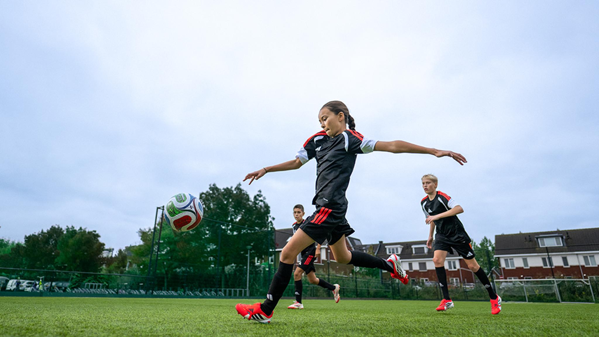 A young person in a soccer uniform kicks a ball on a green field.