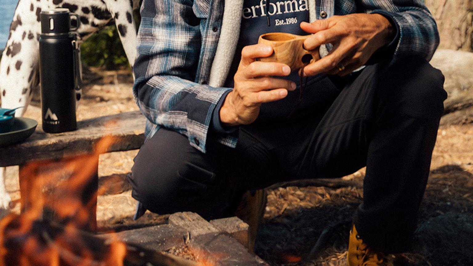 a man in outdoor pants is sitting on a bench holding a cup of coffee .