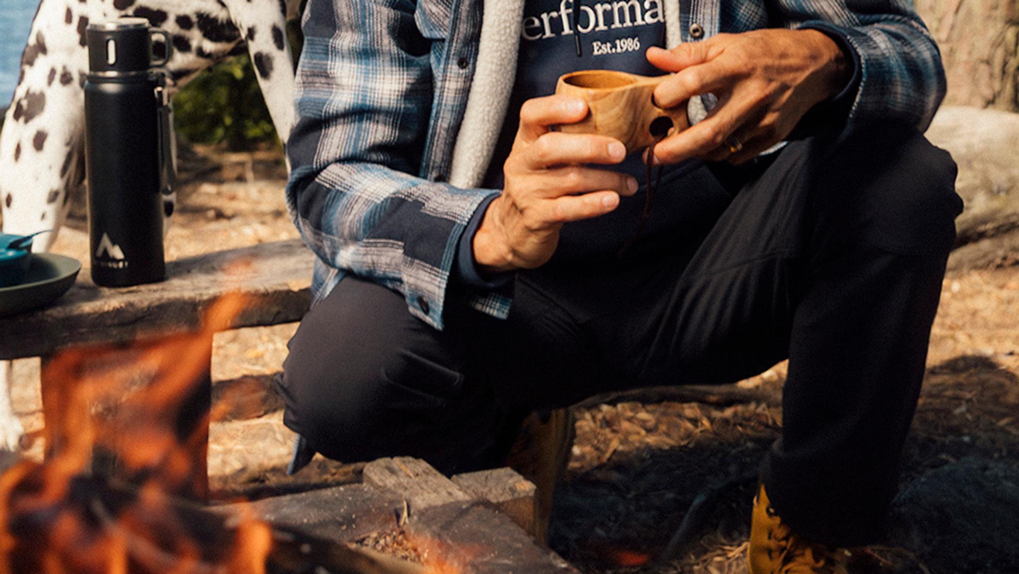 a man in outdoor pants is sitting on a bench holding a cup of coffee .