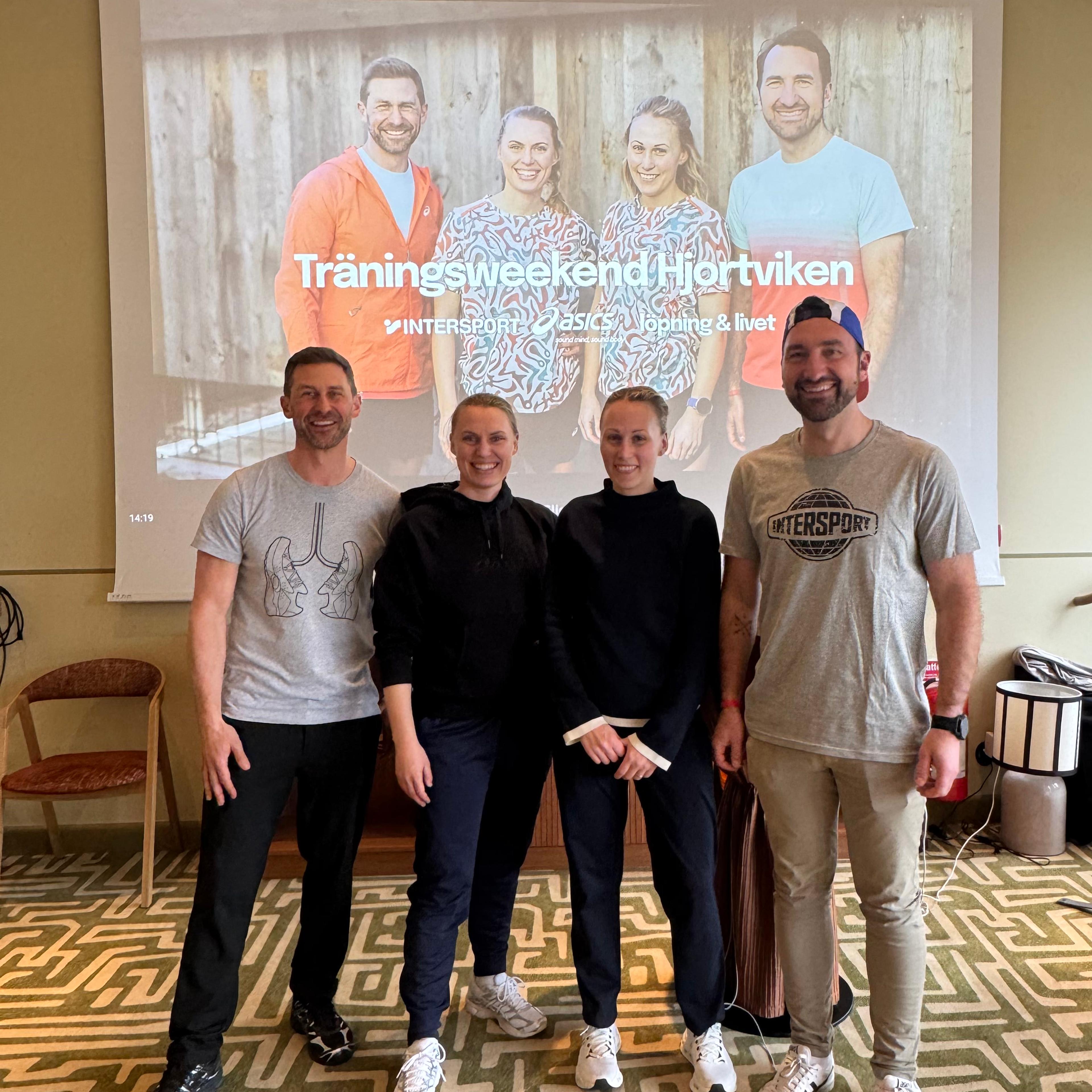 Four smiling people stand in front of a projector screen displaying an event banner for "Träningsweekend Hjortviken" with Intersport and ASICS logos.