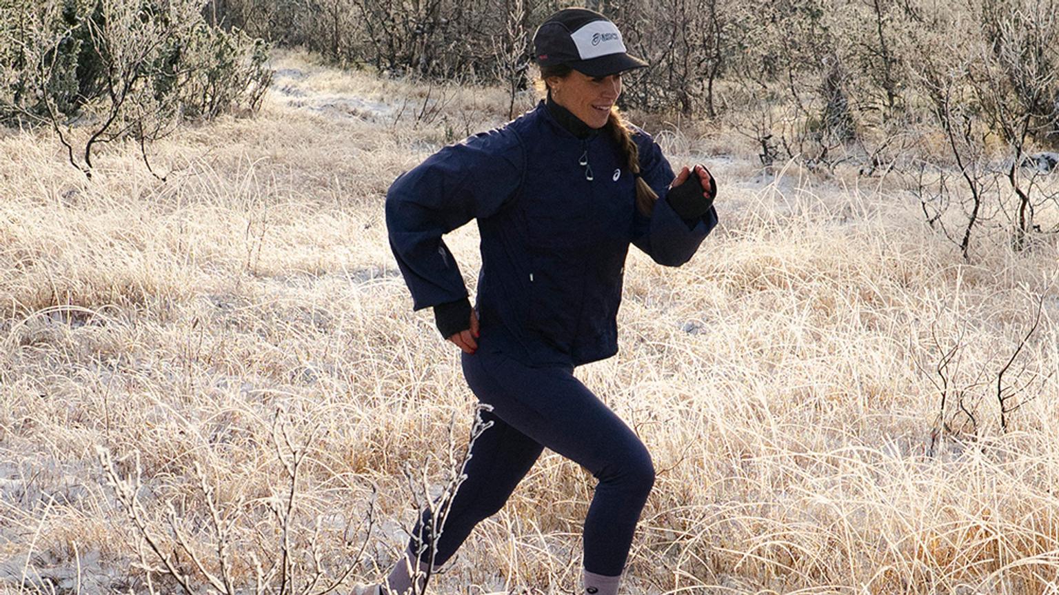 A woman in running gear runs through a field of frosty grass.