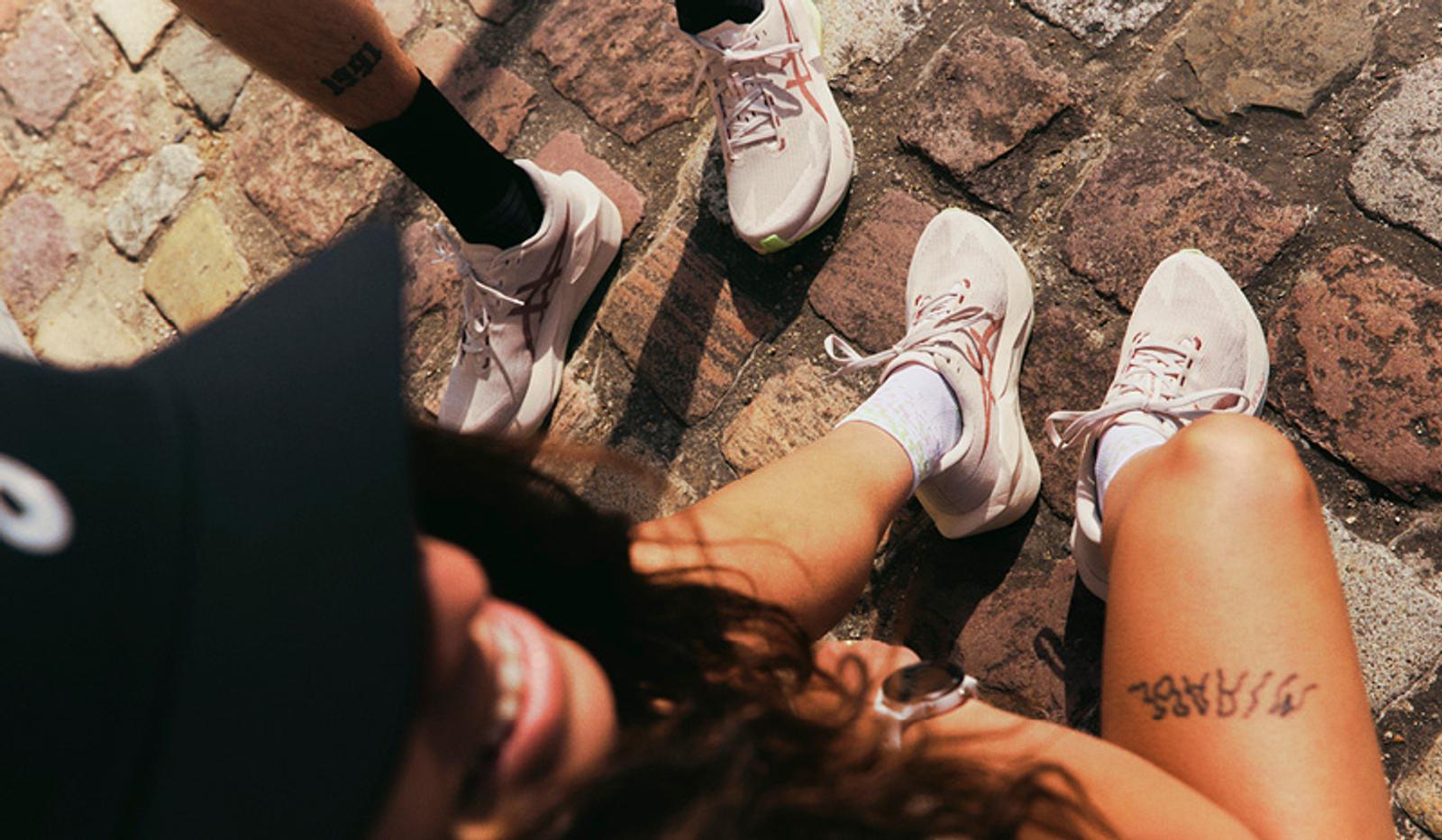 Overhead view of three people wearing sneakers on a cobblestone street, with one person smiling in the lower left.
