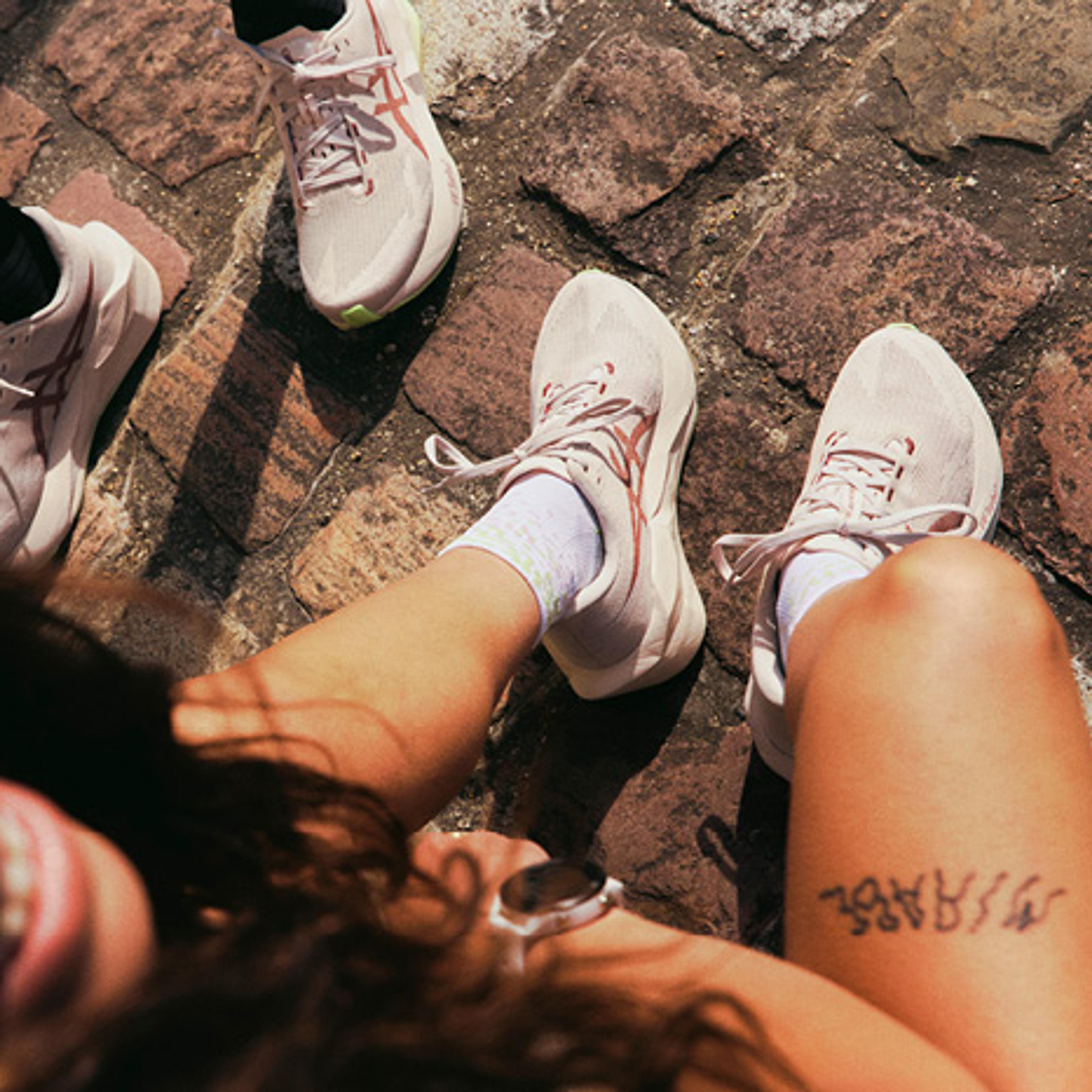 Overhead shot of three people's legs and feet in sneakers on a cobblestone street, one person smiling.