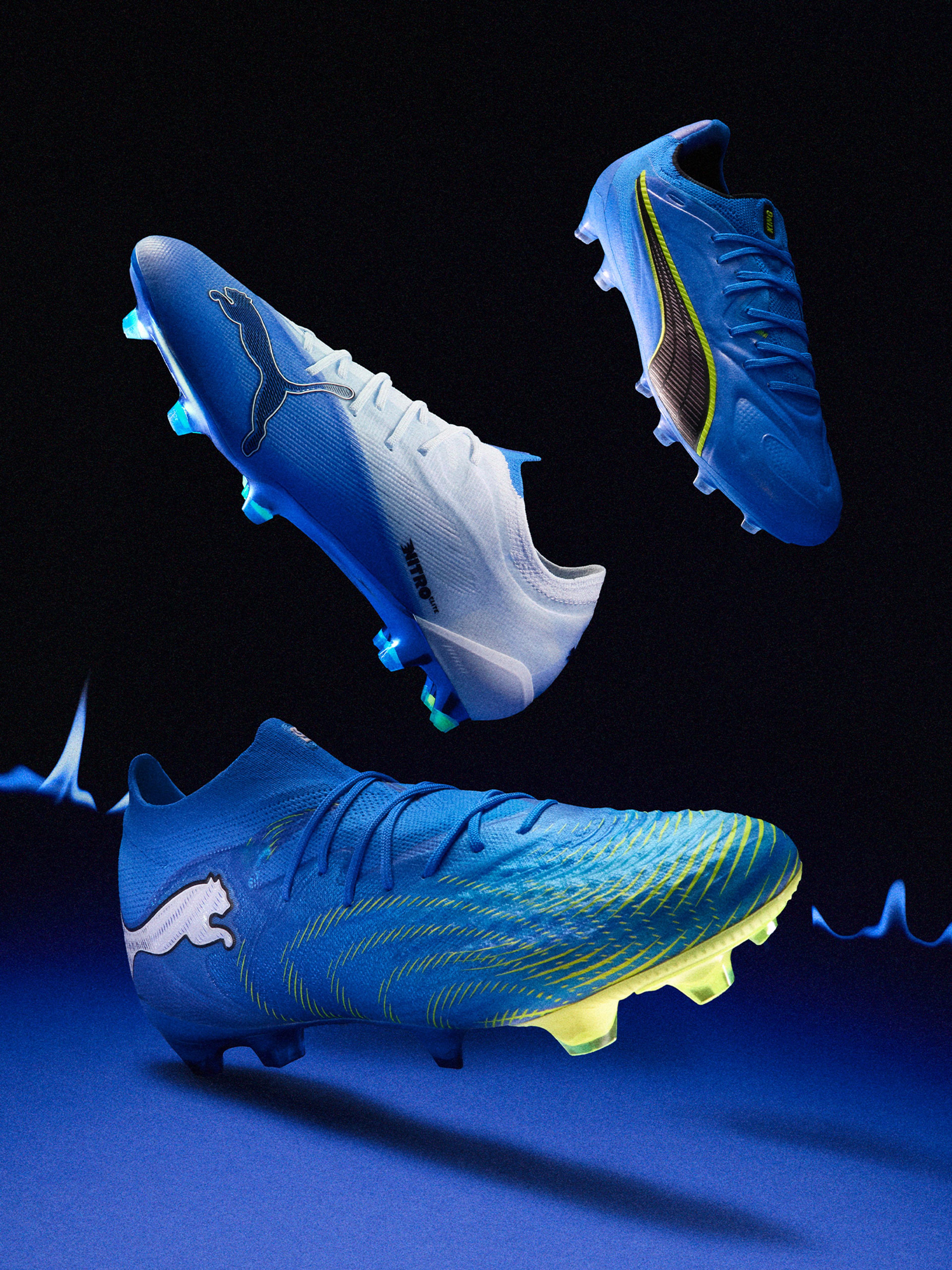 Three Puma soccer cleats in various shades of blue with white, black, and yellow details, illuminated by blue light on a dark background.