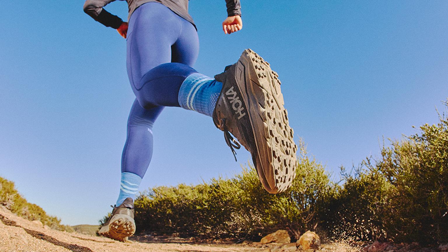 a person is running on a dirt road wearing a pair of hoka running shoes .