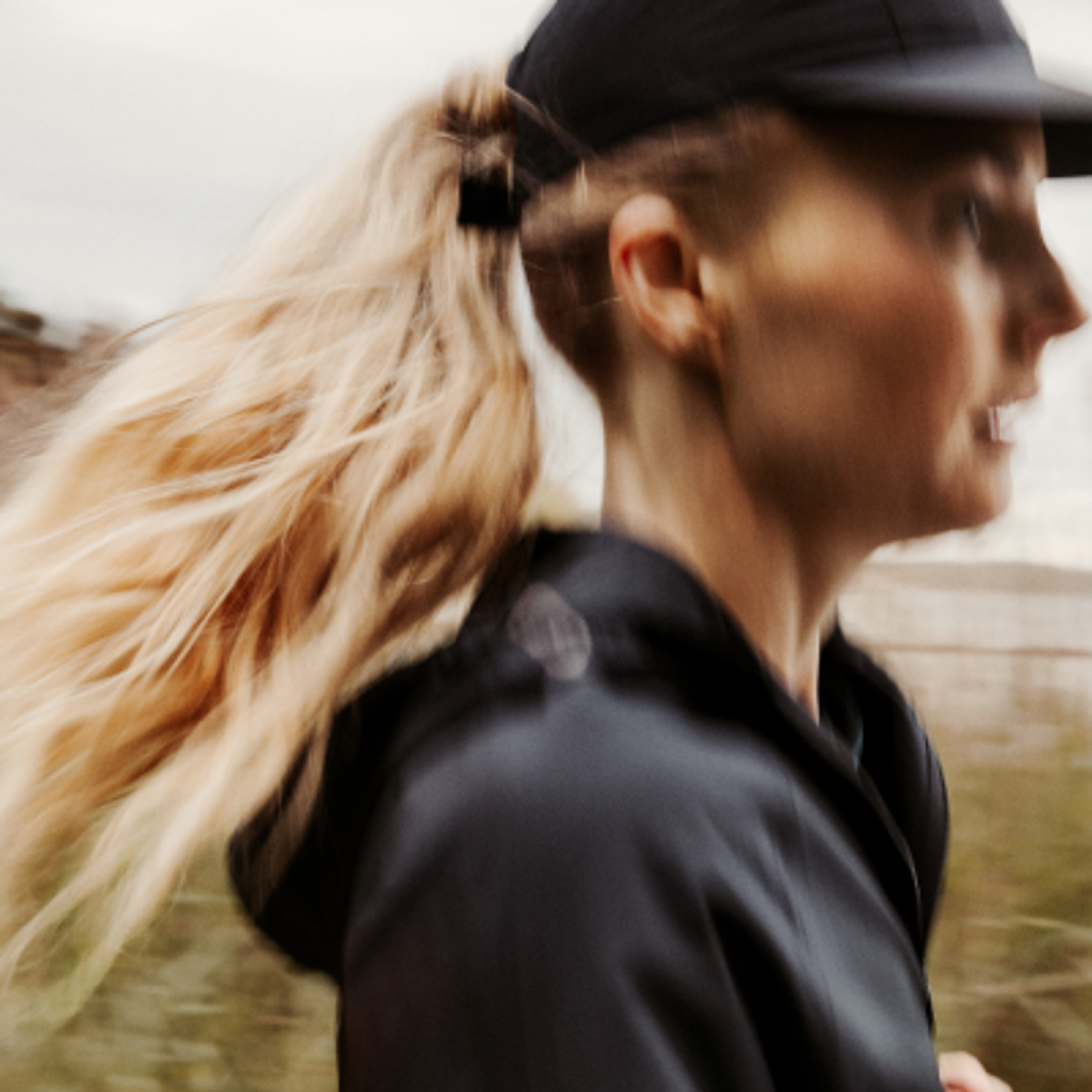 Motion-blurred woman with blonde ponytail, black cap, and jacket.