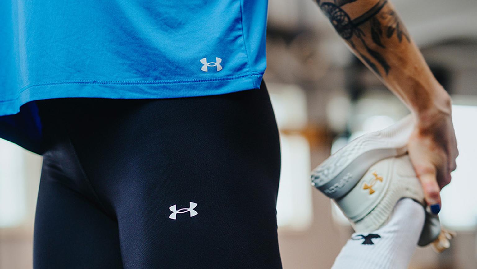 a woman in a blue shirt and black under armour tights is stretching his leg .