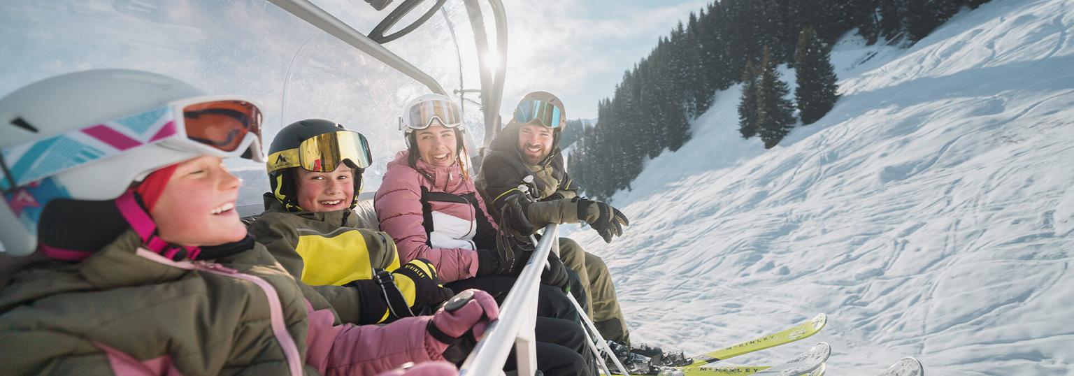 En familj på fyra sitter i en sittlift med skidkläder på sig