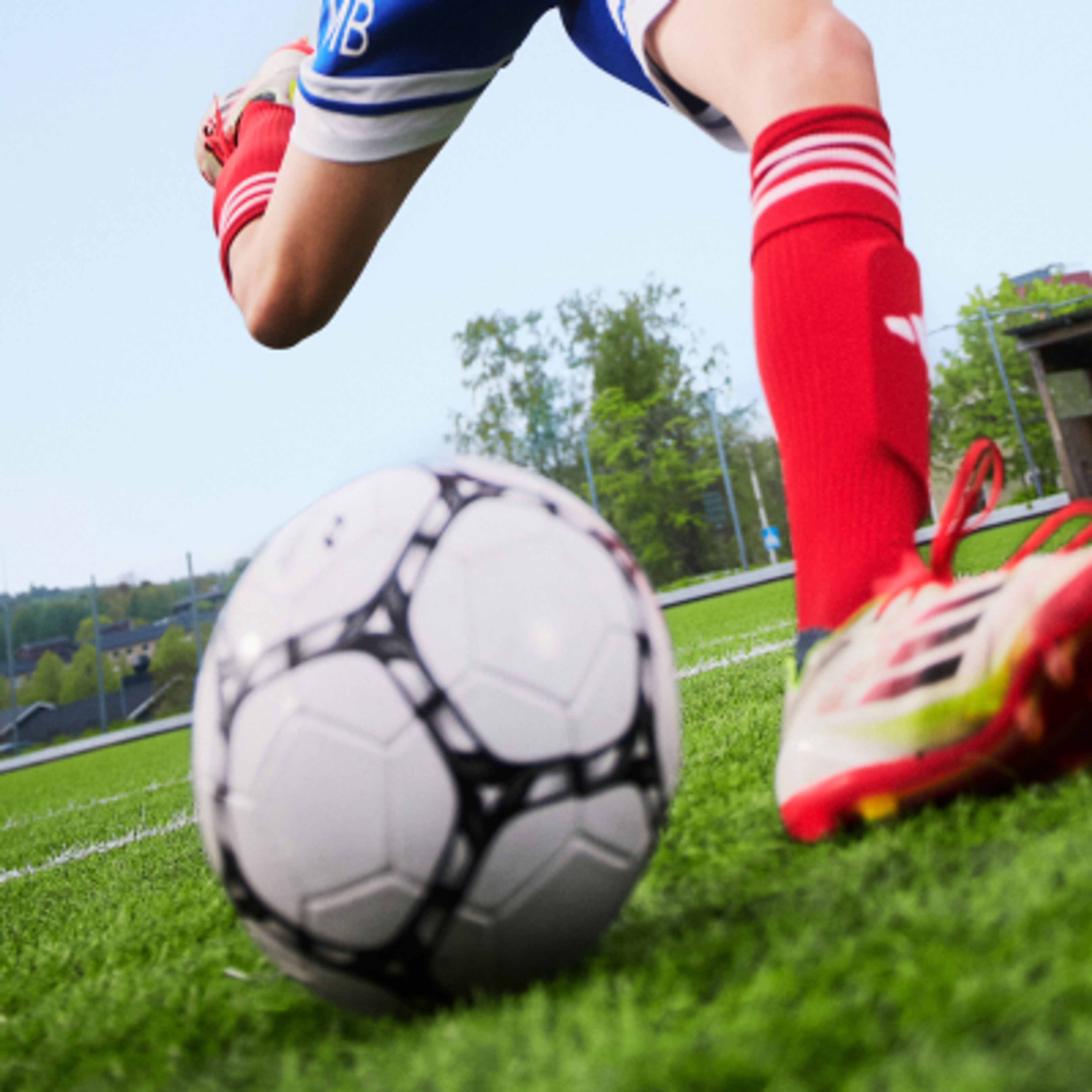 A soccer player's legs in red socks and cleats, with one foot lifted over a soccer ball on a green field.
