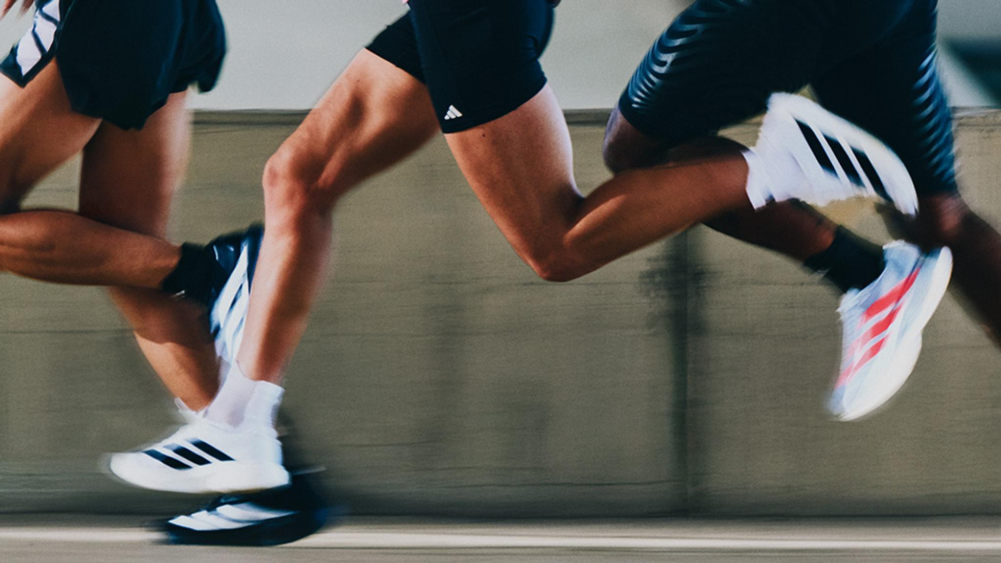 Runners' legs in motion, wearing Adidas shorts and running shoes, with speed blur.