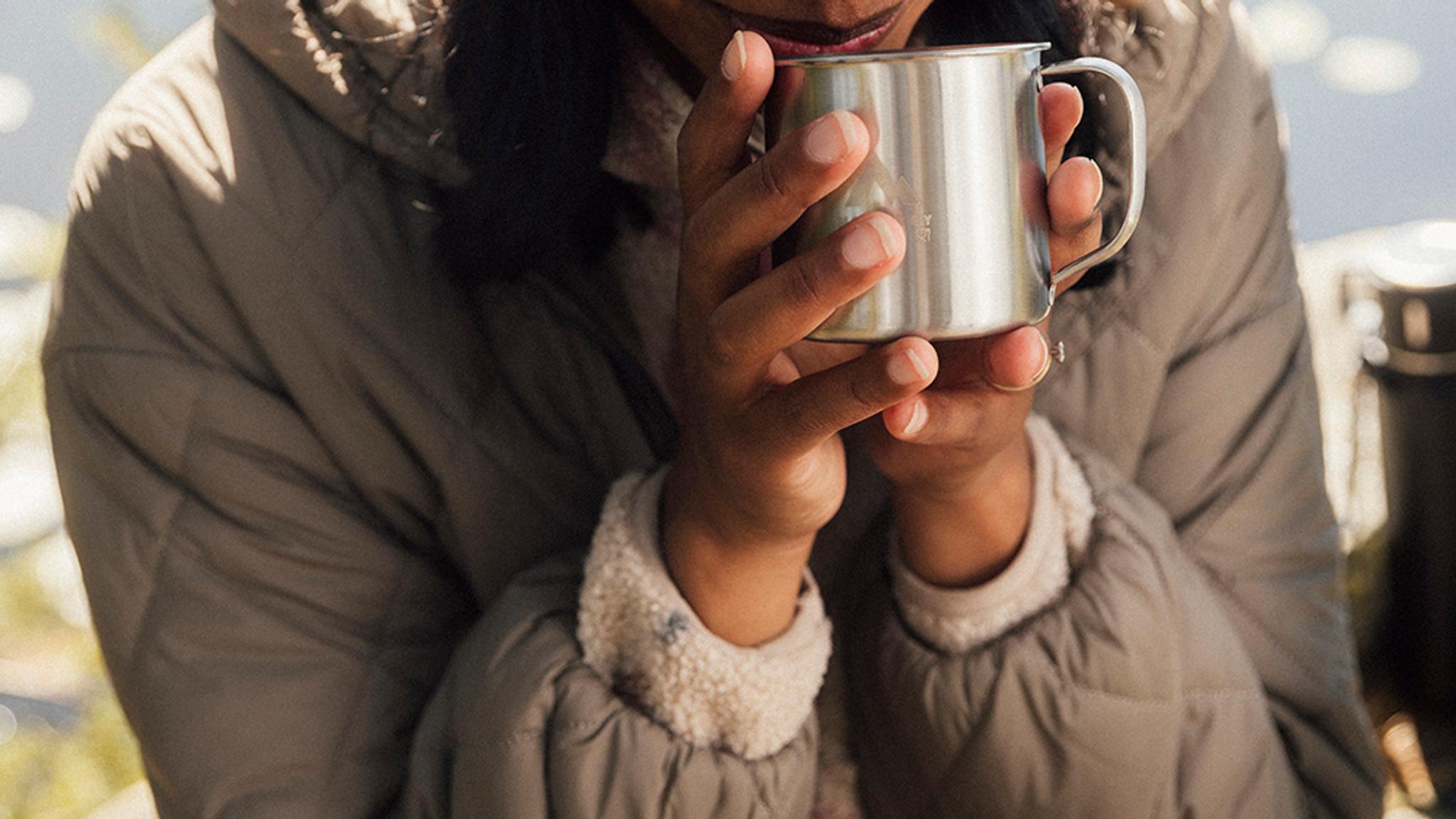 a woman in a new jacket is drinking from a stainless steel mug .