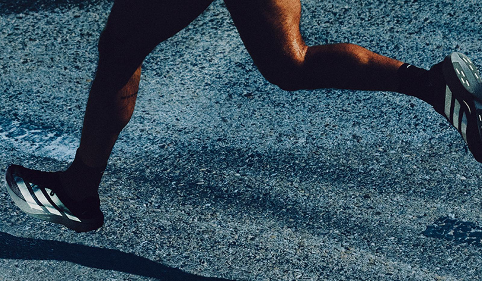 Close-up of a runner's legs and feet in striped athletic shoes on a textured road.