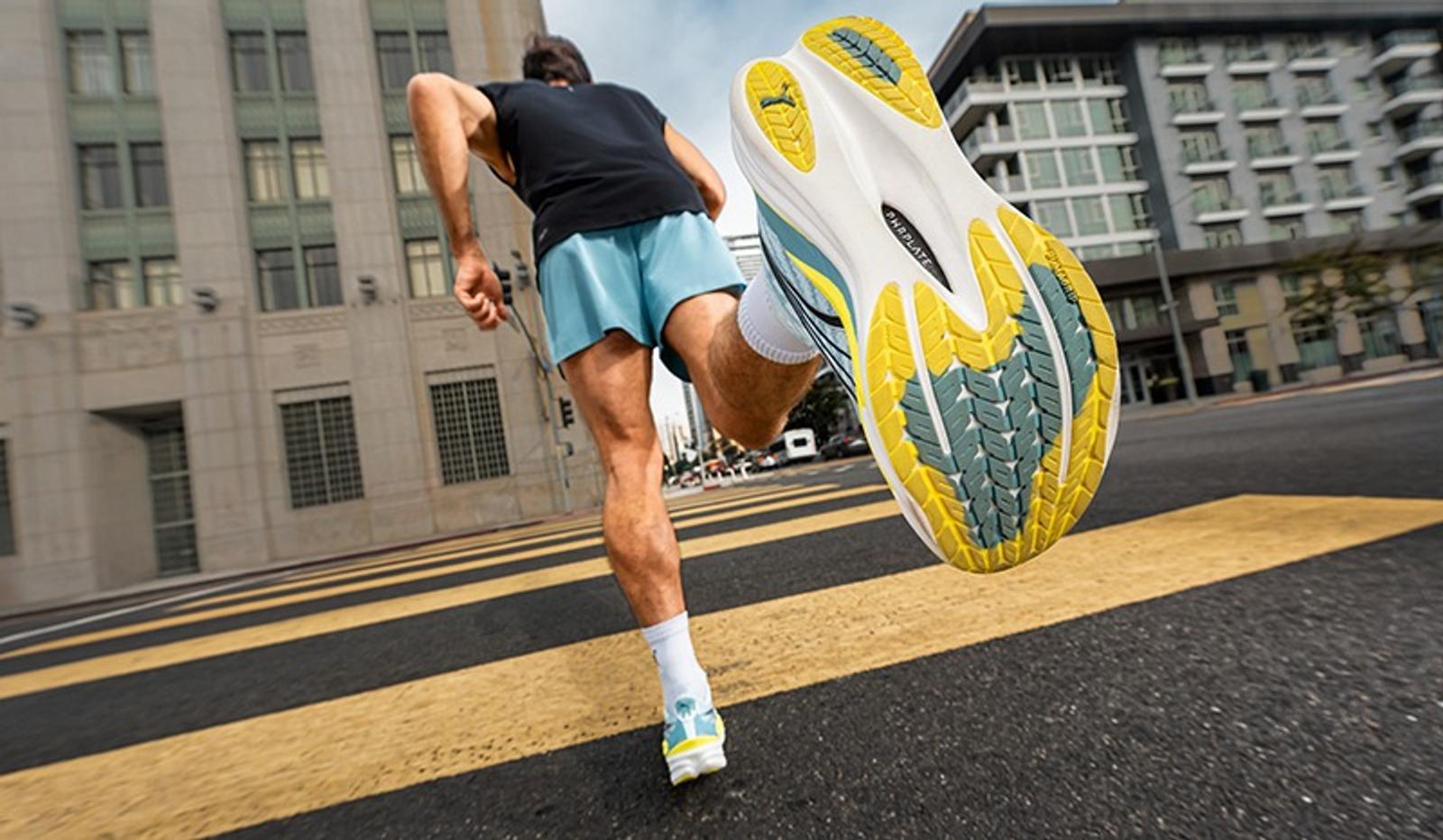 Runner on a city street, with one foot raised showing the yellow, blue, and white sole of their shoe.
