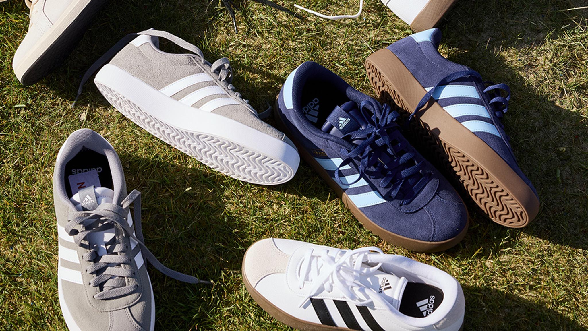 Multiple pairs of Adidas sneakers in different colors on green grass.