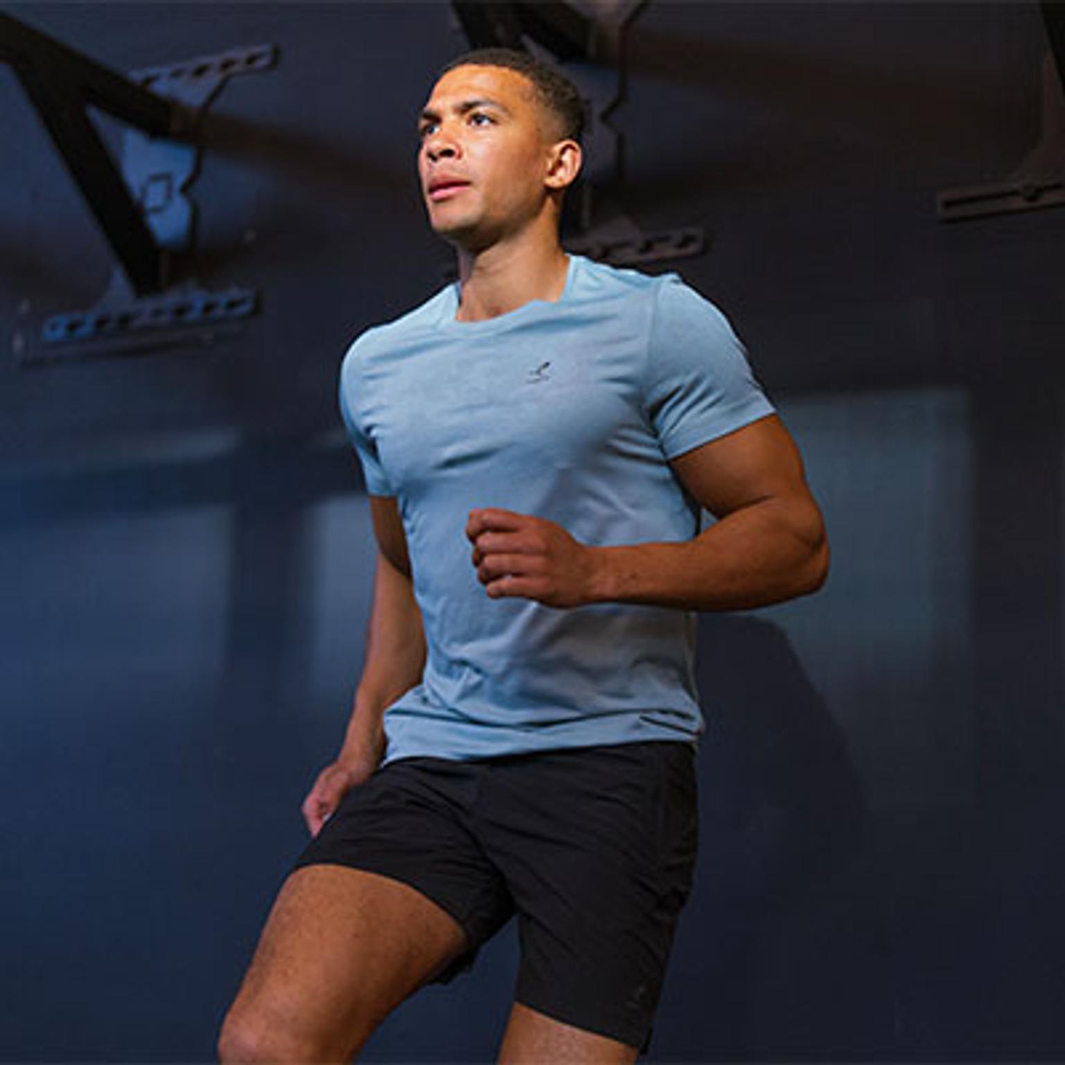 a man in a blue shirt and black shorts is running in a gym .