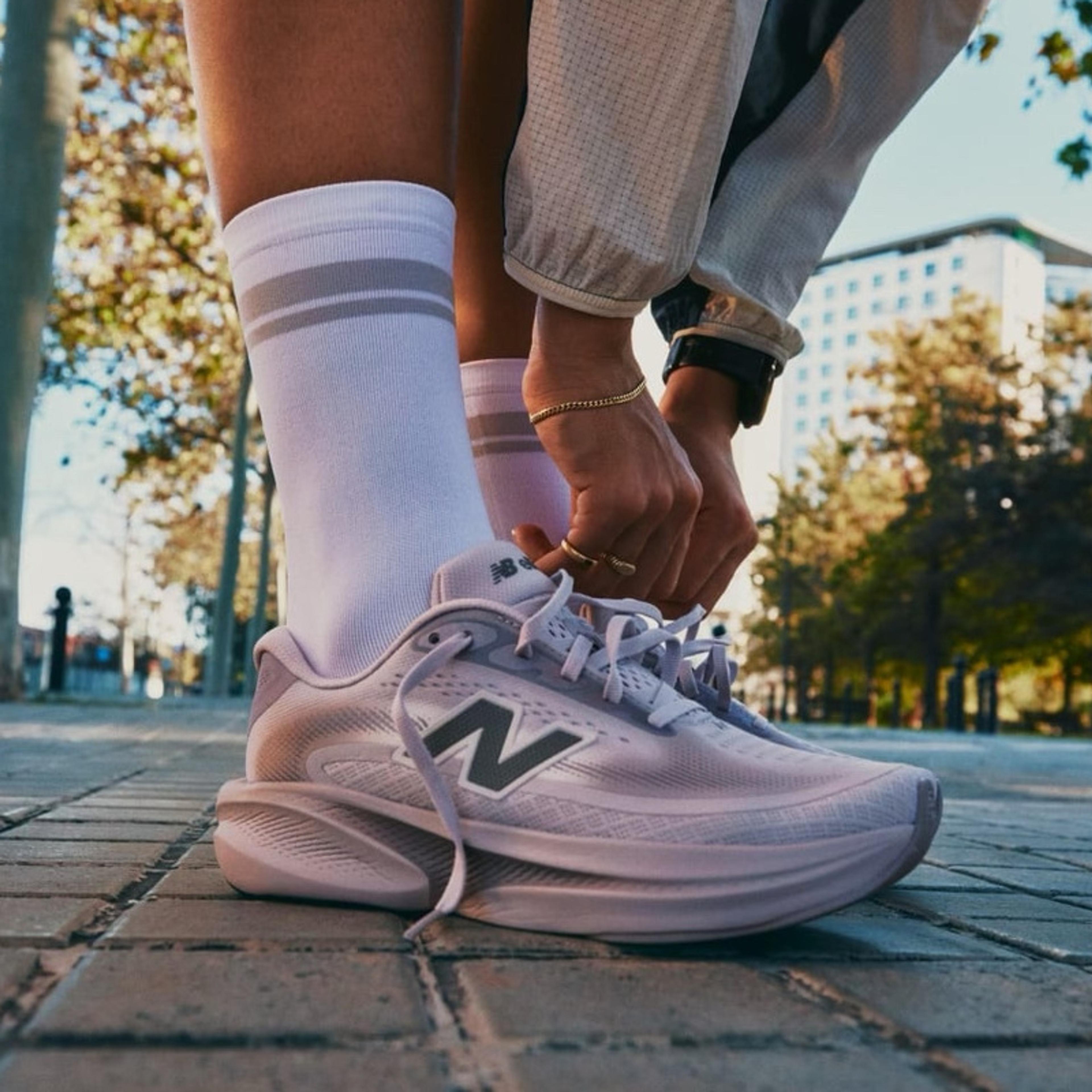 A person tying the laces of a light purple New Balance running shoe on a paved path.