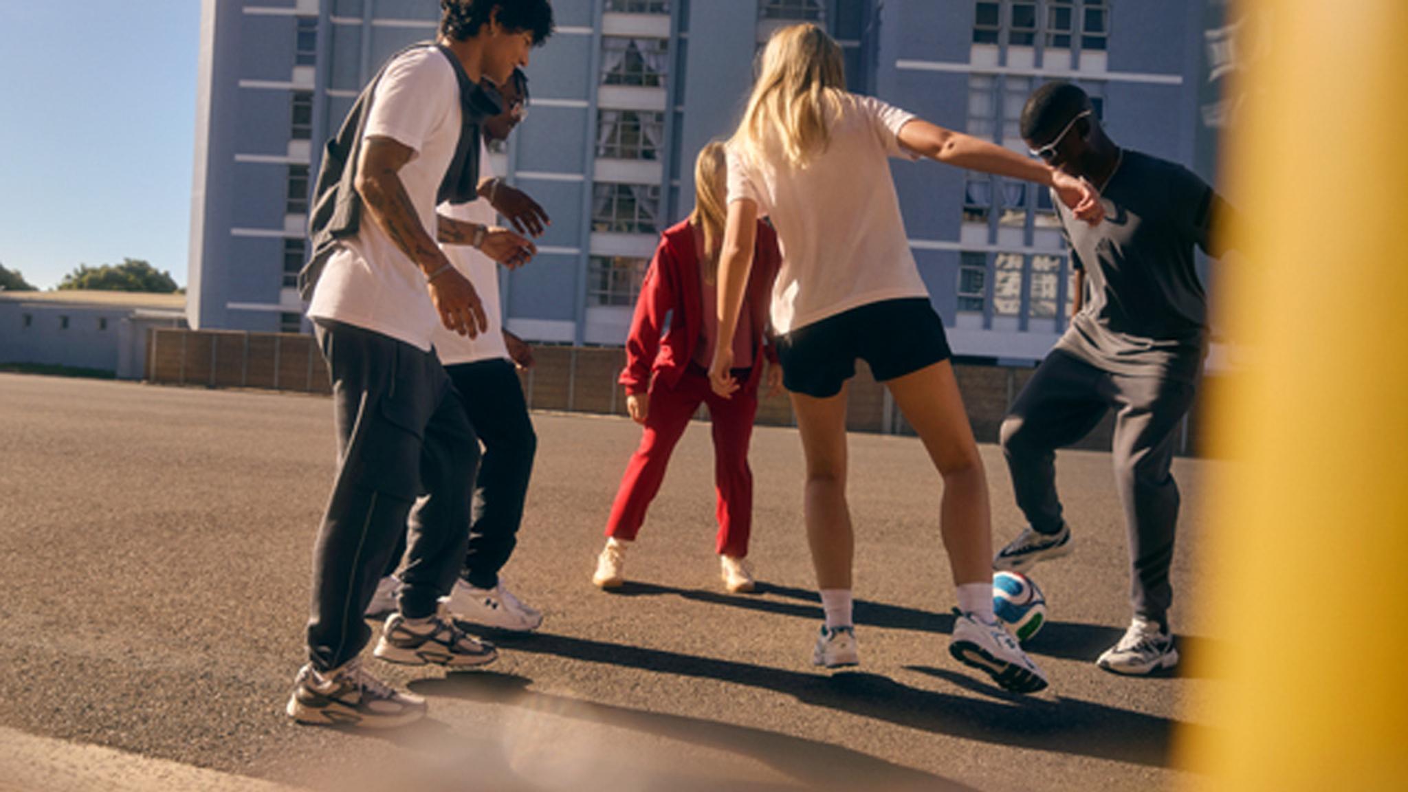 A diverse group of young adults playing soccer on an urban street.