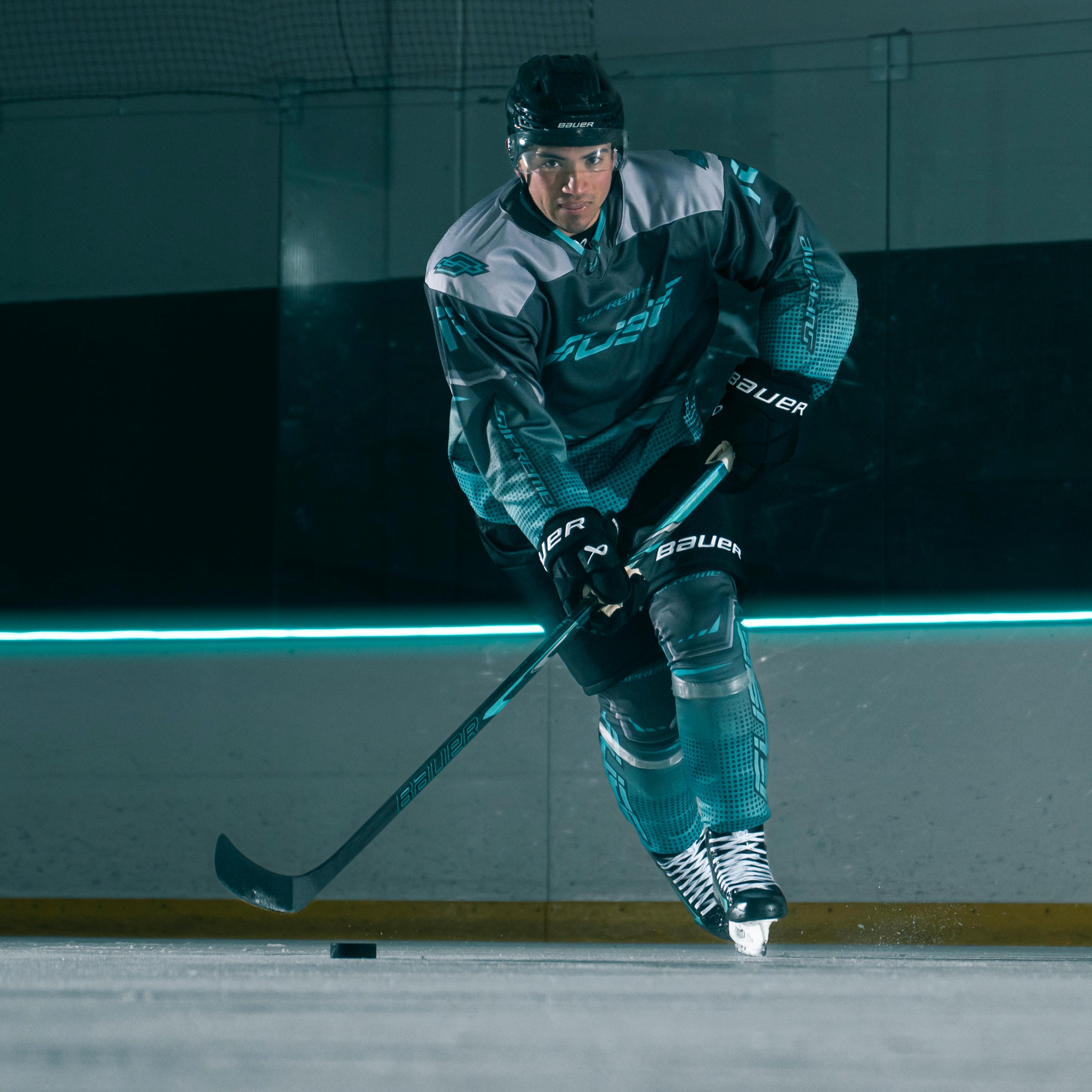 Ice hockey player skating with a puck on a rink, with a blue neon light line on the wall.