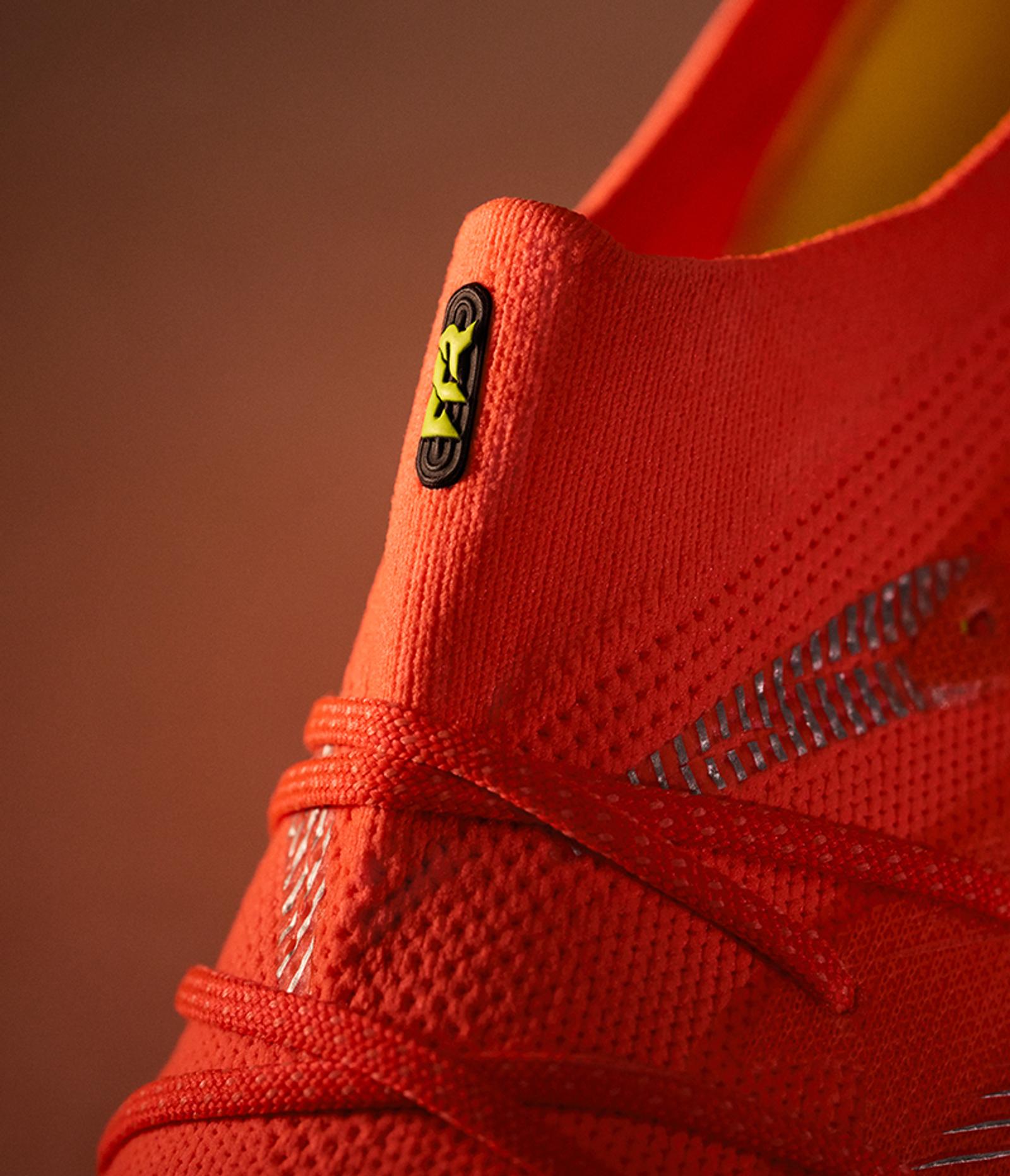 Orange knit athletic shoe with laces and a black and yellow logo on its ankle collar.