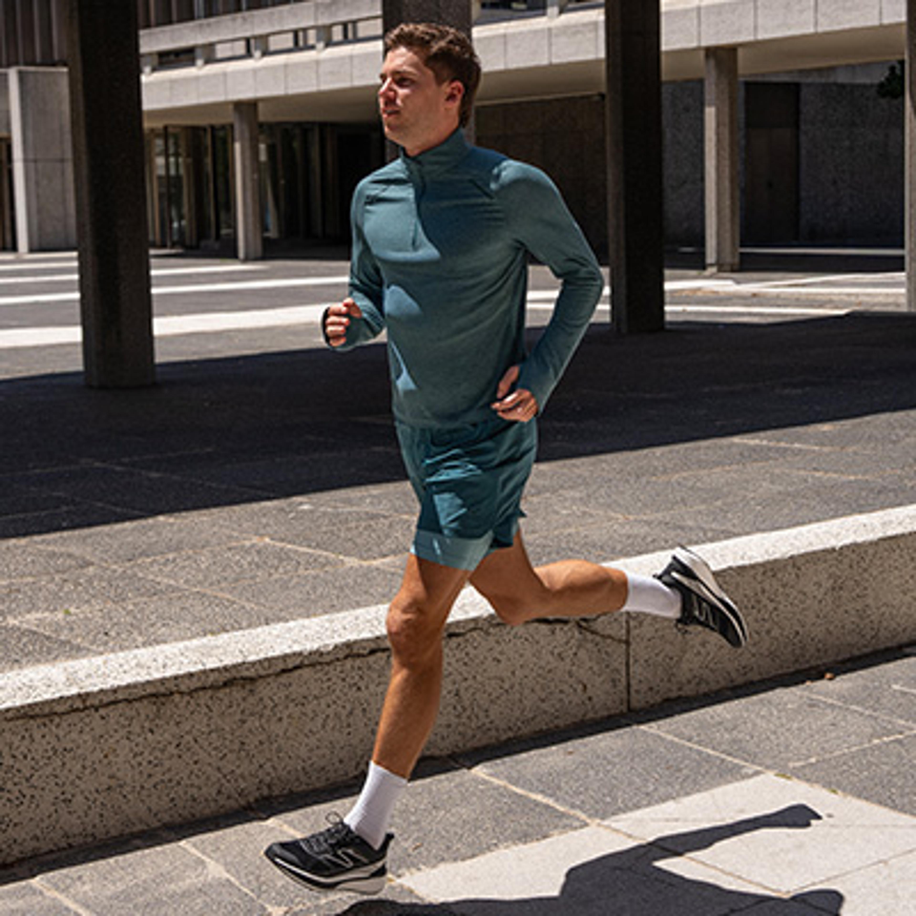 A man in a teal long-sleeved running shirt and shorts runs outdoors.
