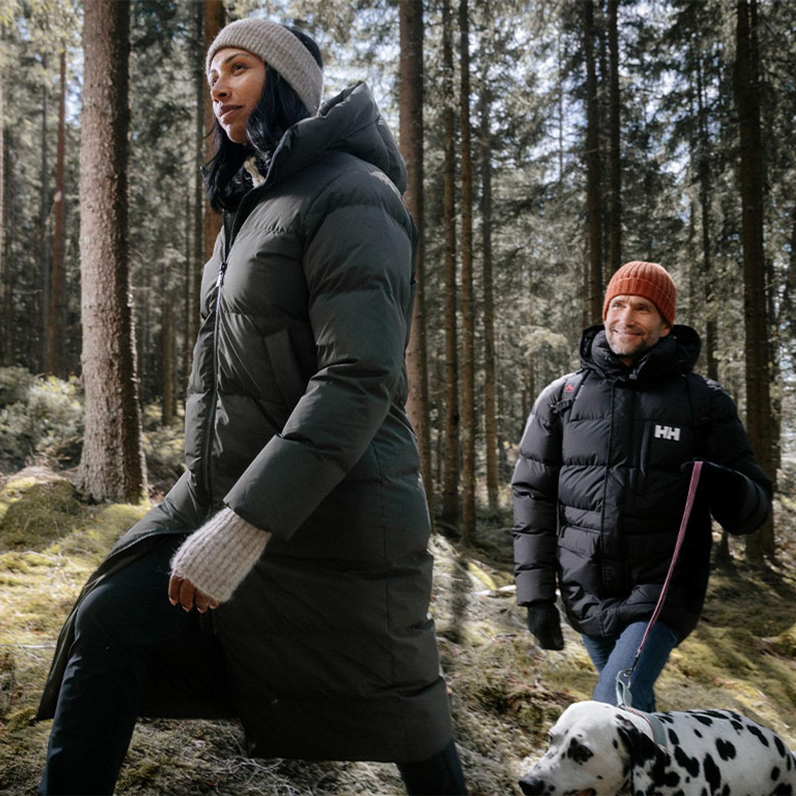 a man and a woman are walking a dalmatian dog in the woods .