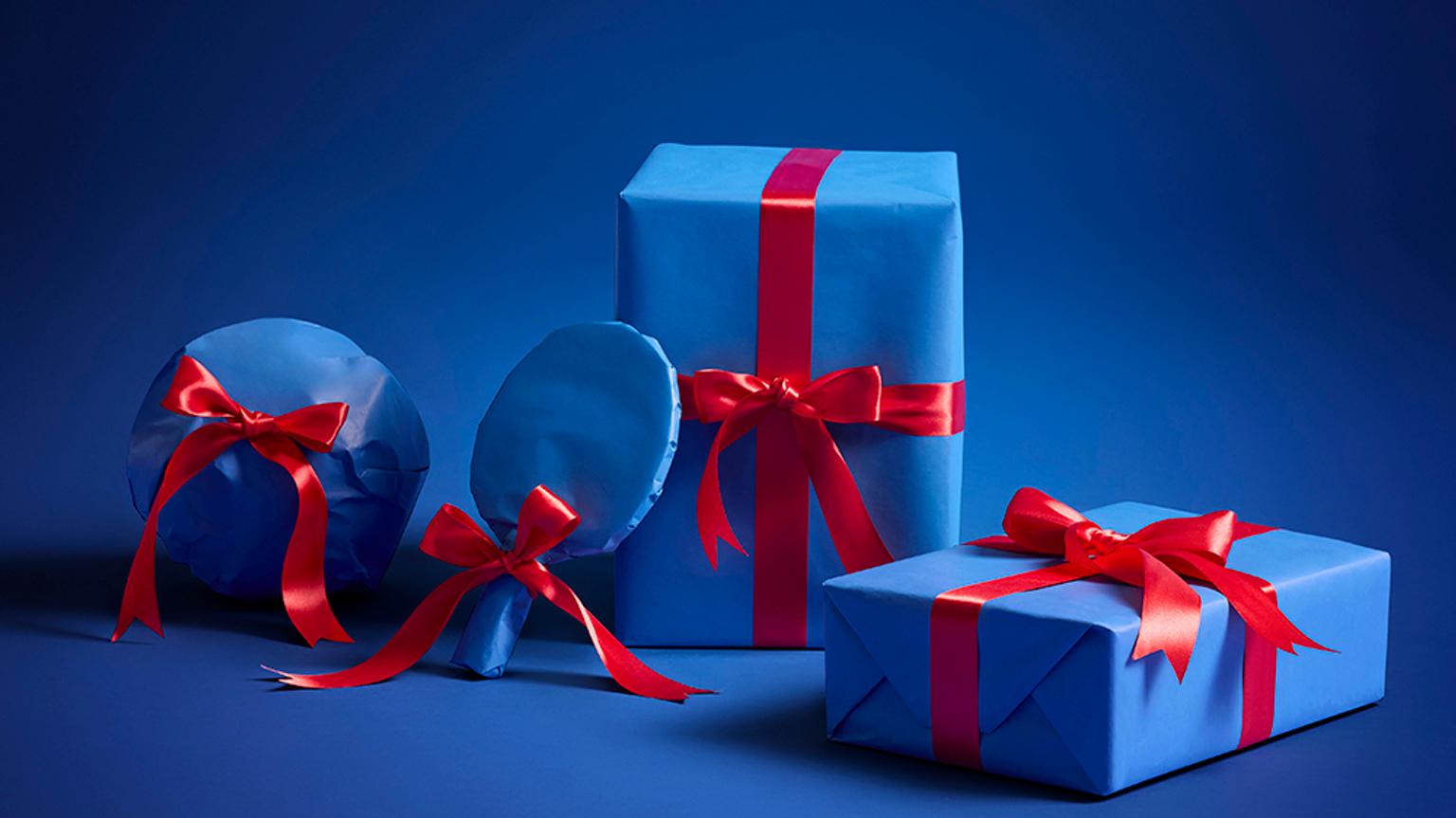 Four sporty gifts wrapped in blue paper with red ribbons on a blue background.