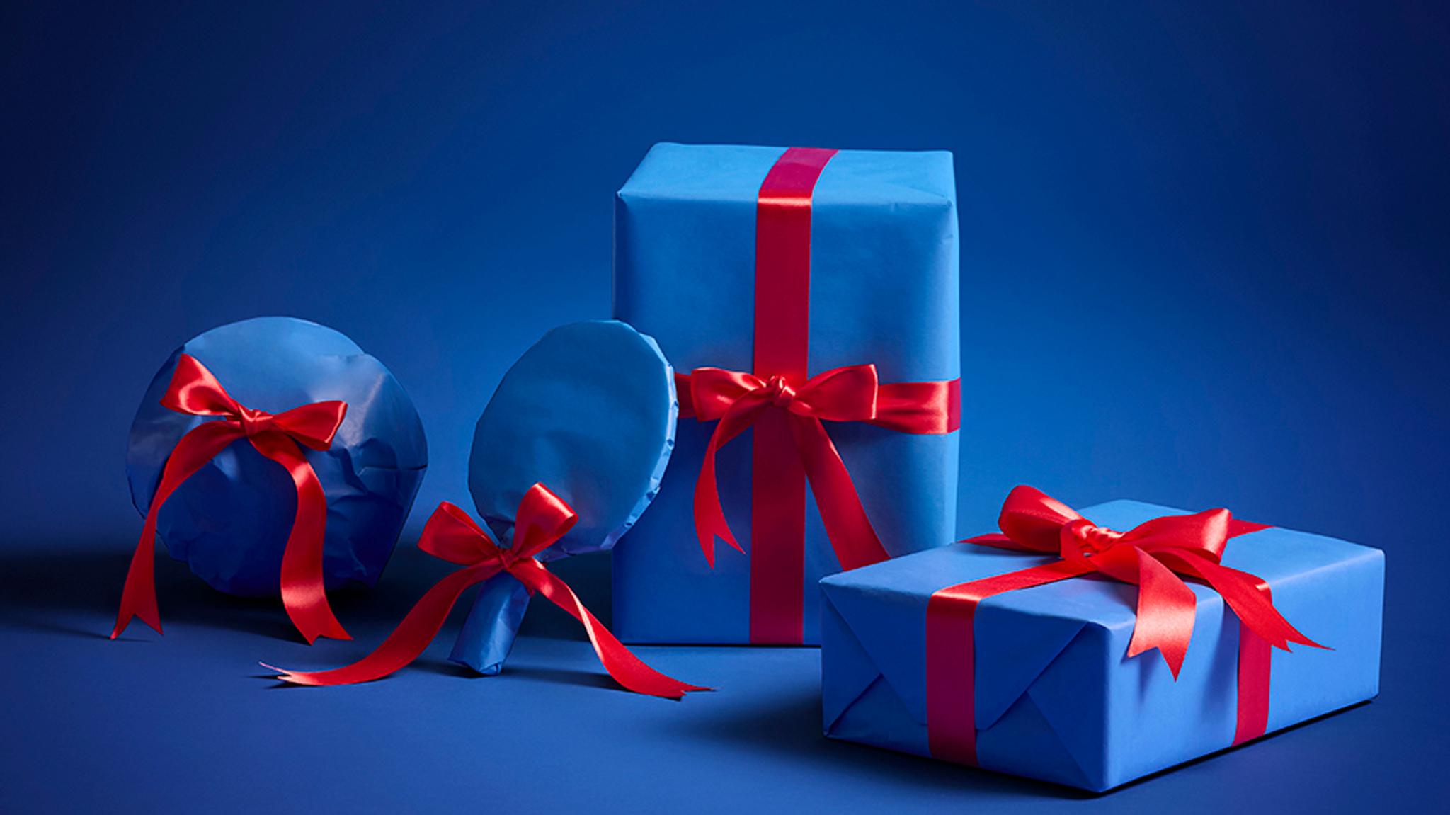 Four sporty gifts wrapped in blue paper with red ribbons on a blue background.