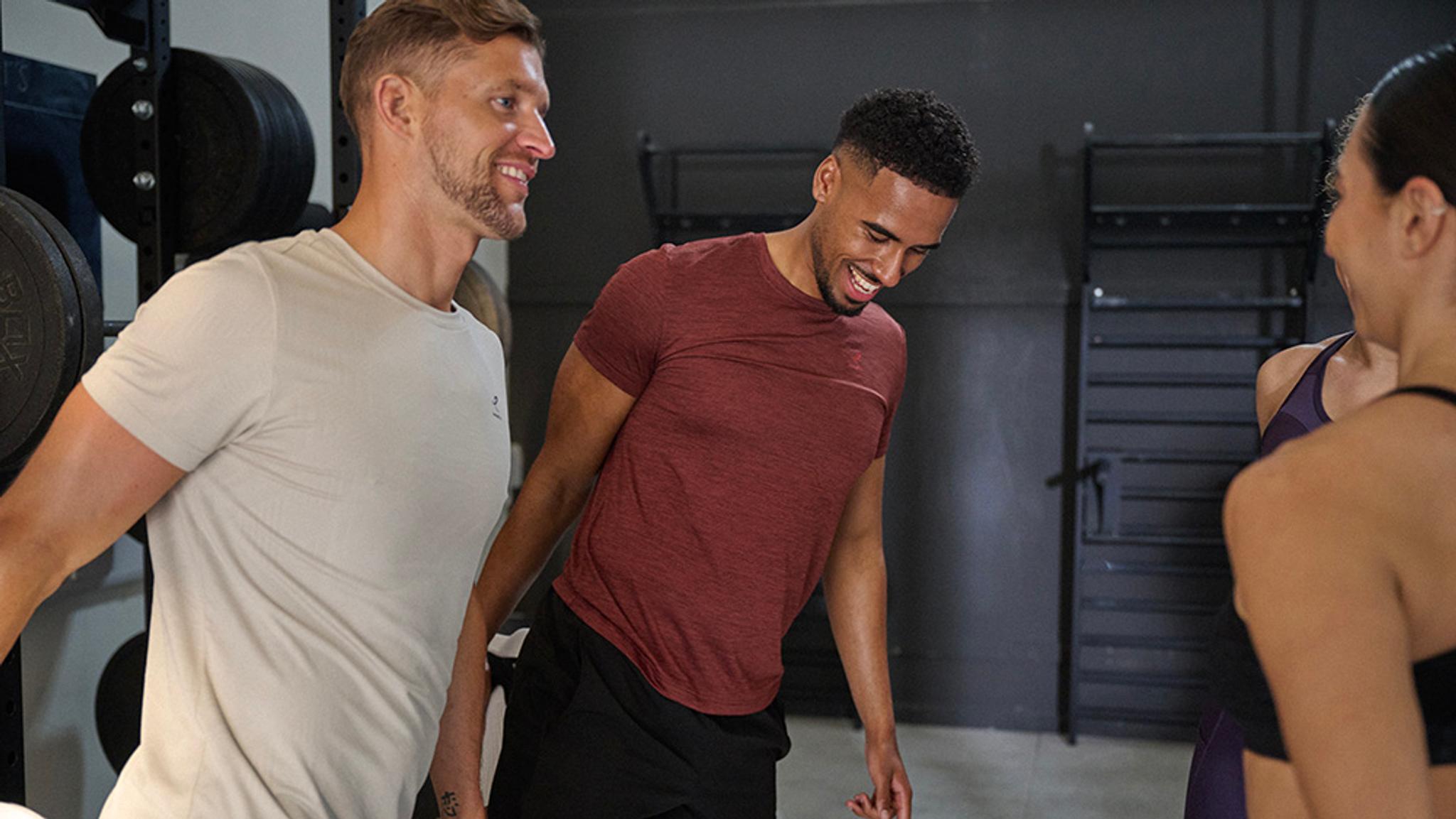 Two men and a woman is stretching, smiling and talking in a gym.
