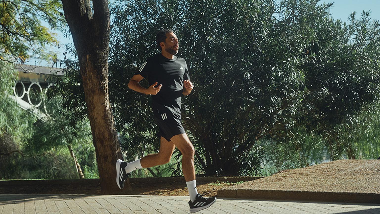 a man is running on a sidewalk next to a tree .