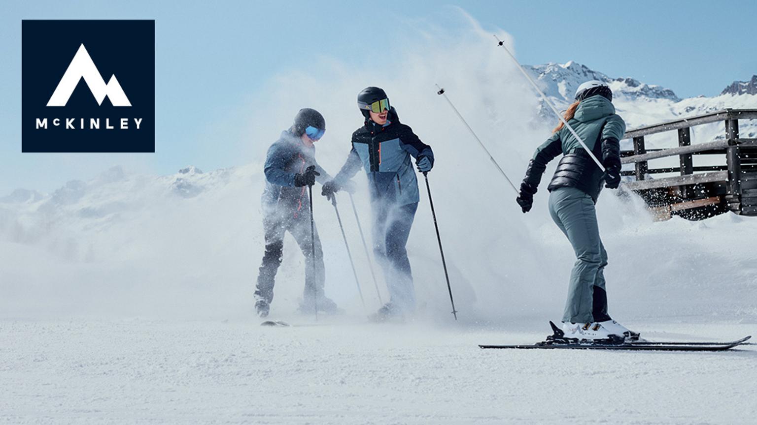 Three skiers kicking up snow on a mountain slope, with the McKinley logo in the top left.