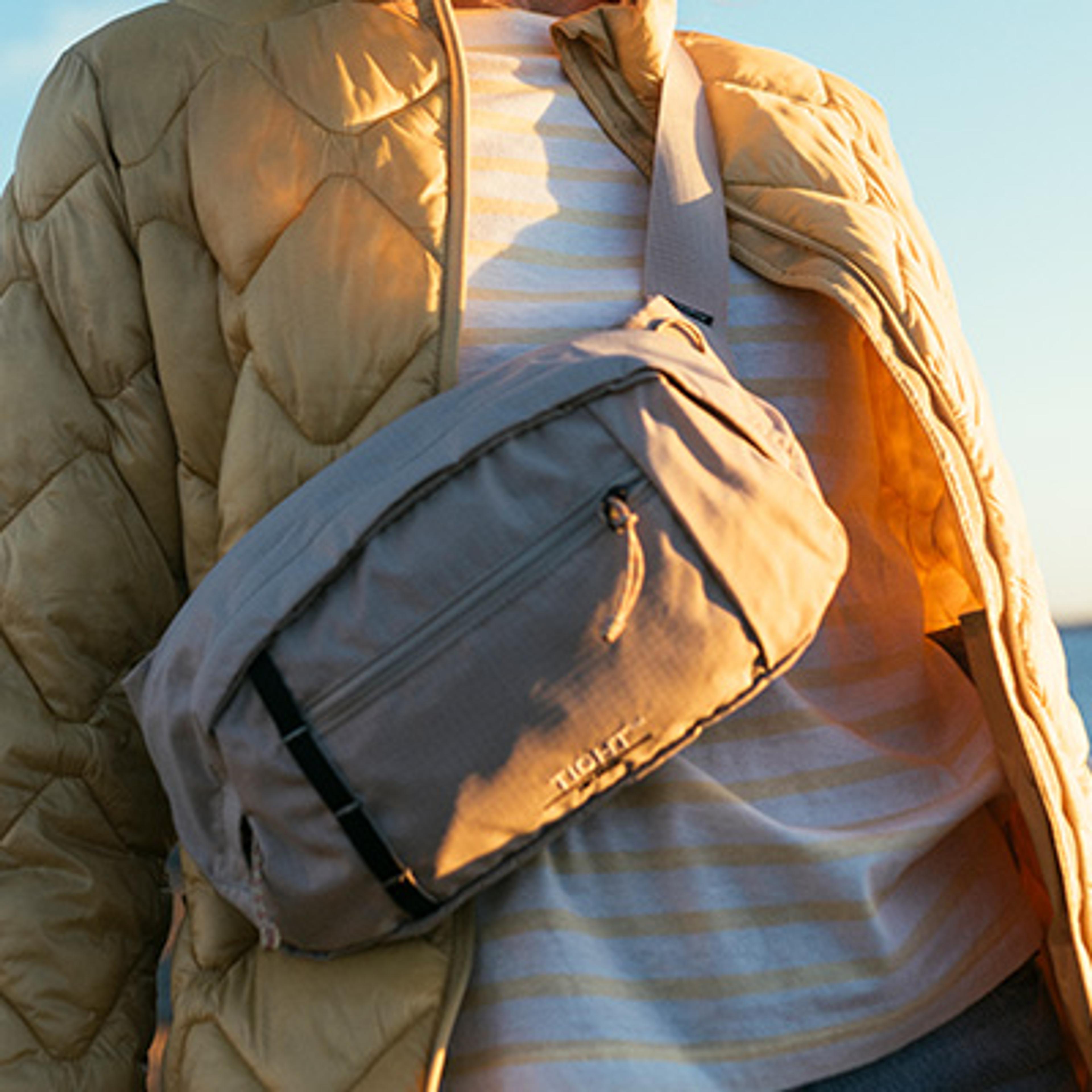 Person wearing a beige quilted jacket and striped shirt, with a beige TIGHT crossbody bag.