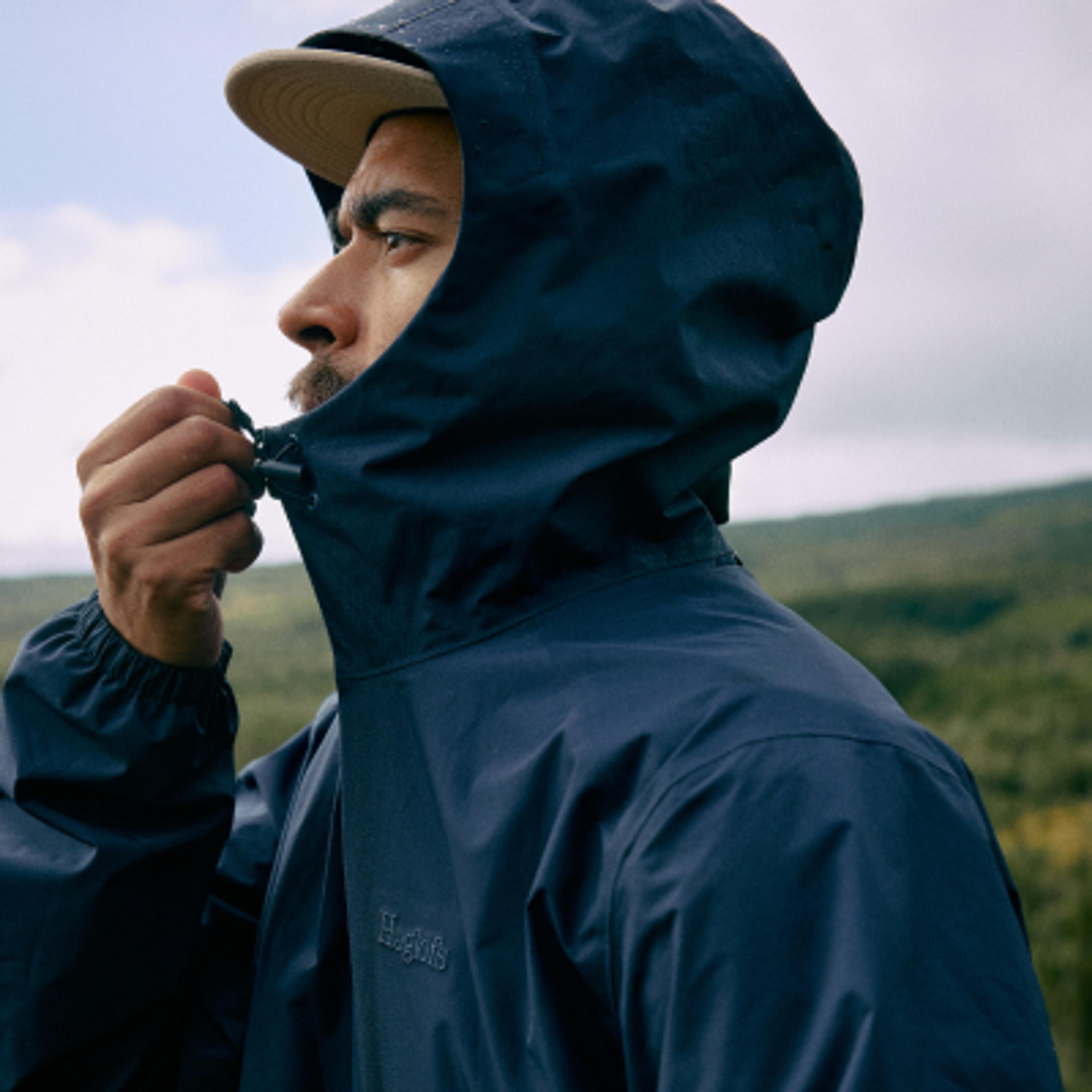 A man in a navy Haglöfs hooded jacket adjusts his hood outdoors.