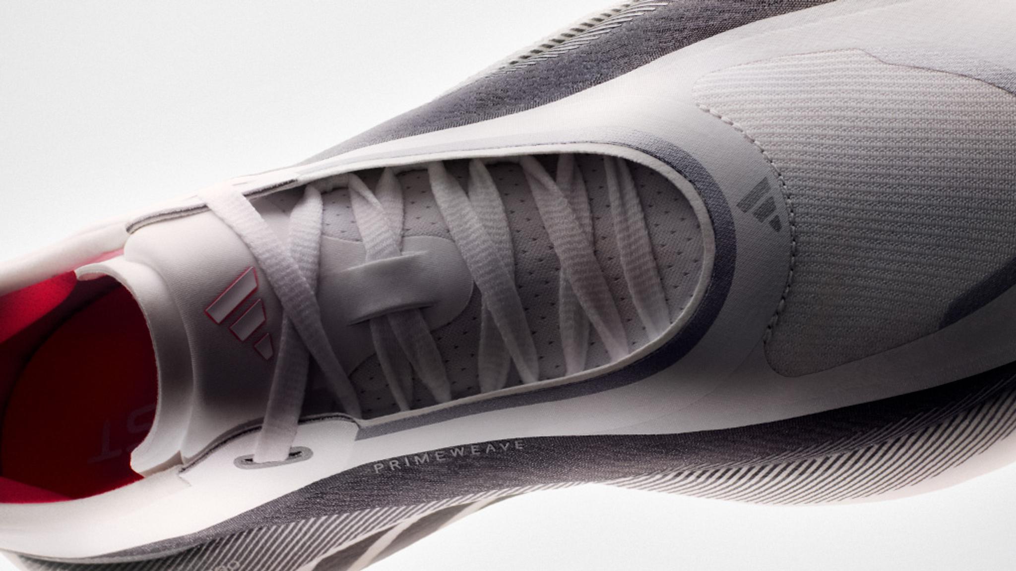 A close-up, top-down view of a grey and white Adidas running shoe with laces, mesh upper, and a pink interior.
