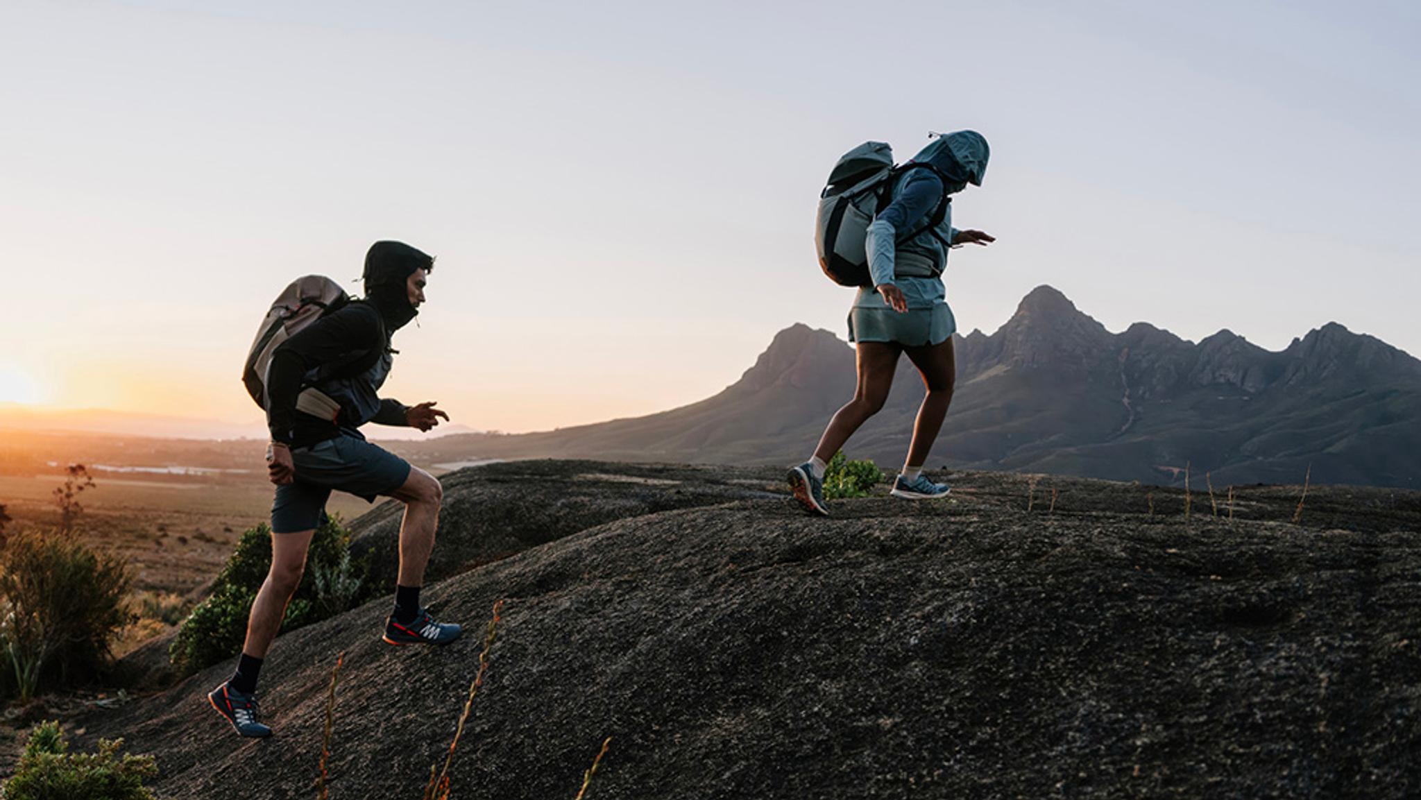 a man and a woman are hiking up a hill .