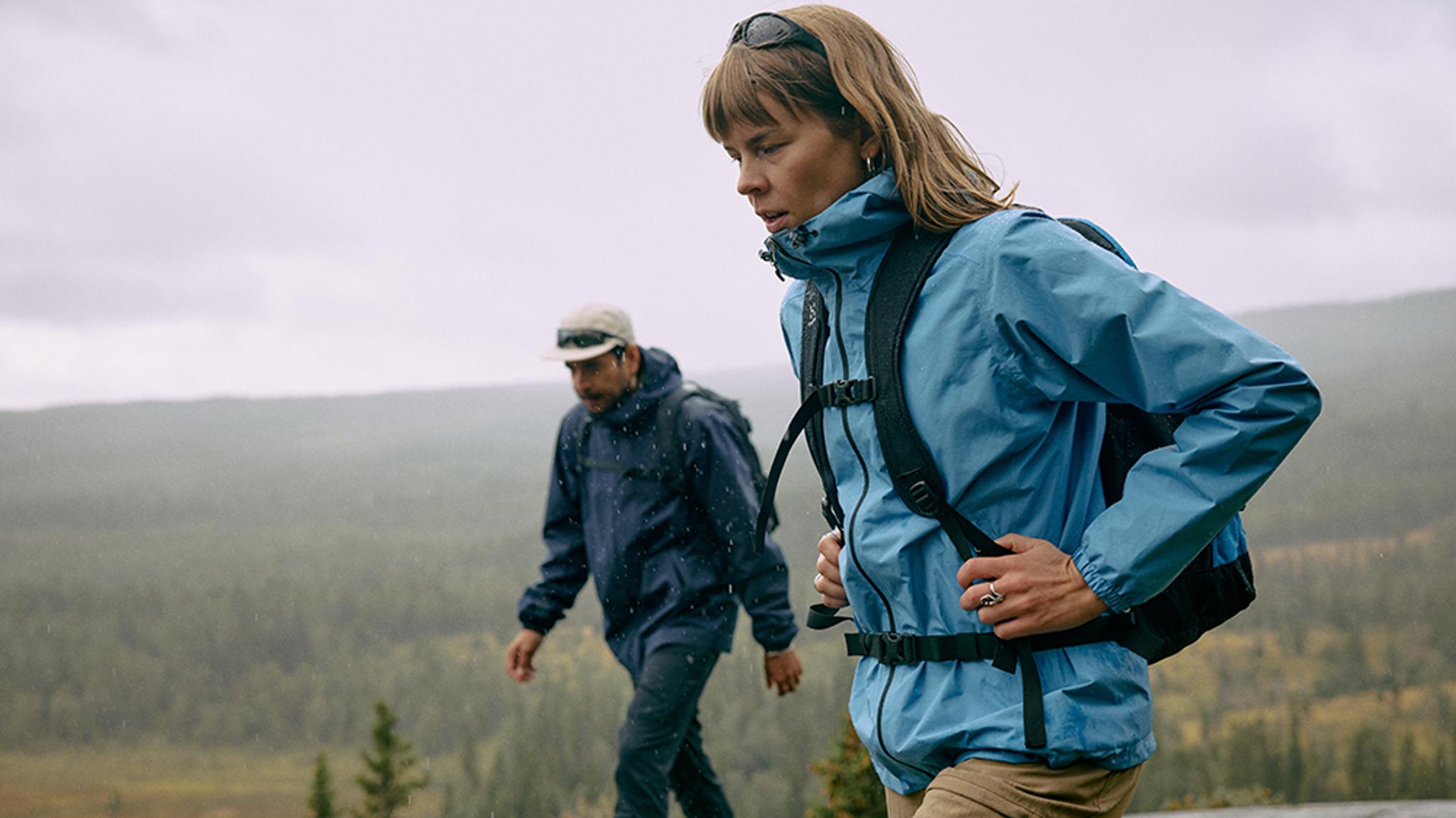 Two hikers in rain jackets and backpacks on a misty, forested landscape.