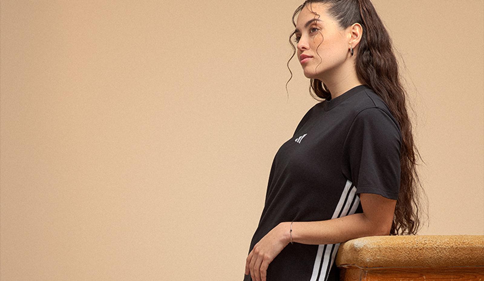 Woman wearing a black Adidas t-shirt with white stripes, leaning and looking left.