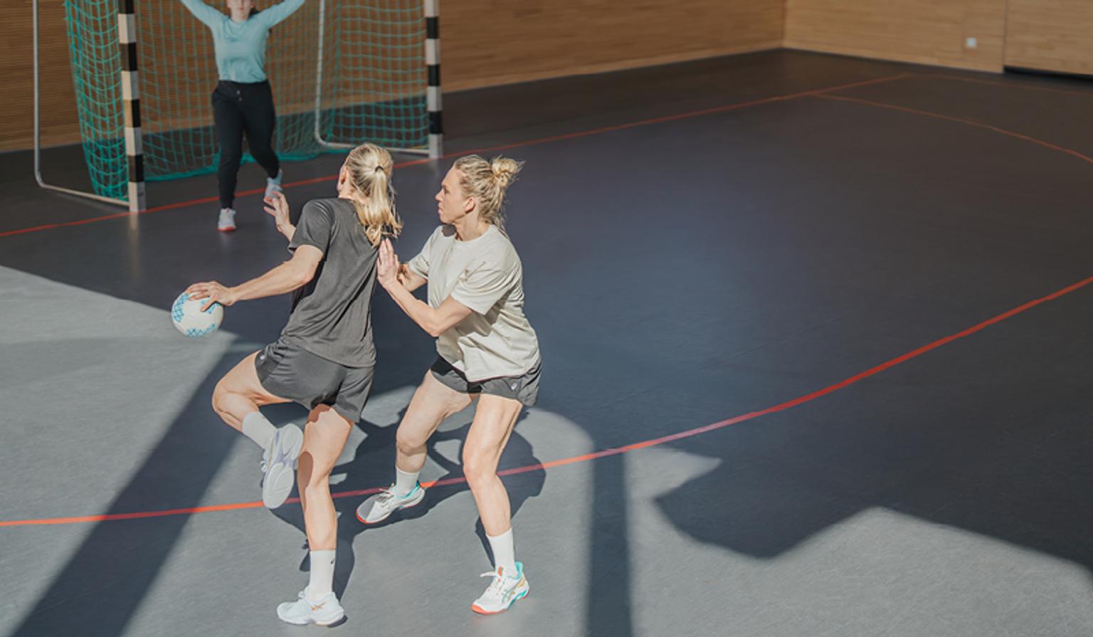 two women are playing handball on a court .