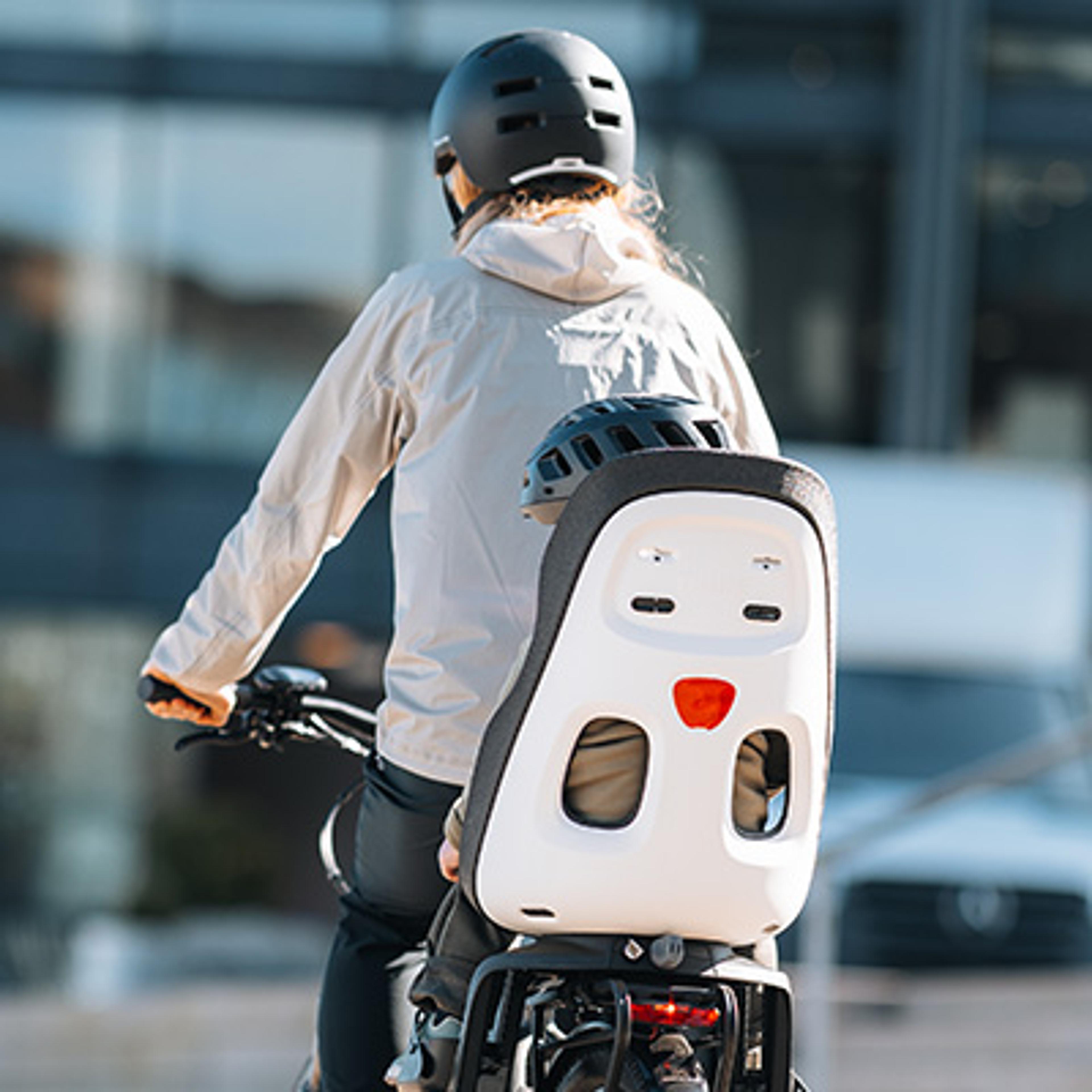 Person on a bike with a child seat and a second helmet on the seat, viewed from behind.